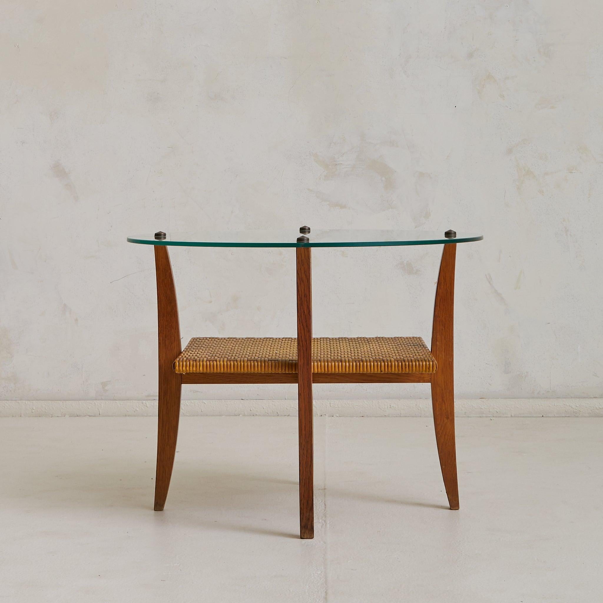 This petite 1960s Italian coffee table features a round glass top delicately poised above a woven rattan shelf. Slender, tapering legs in warm-toned wood anchor the composition, evoking a sense of lightness.

The rattan shelf, with its intricate