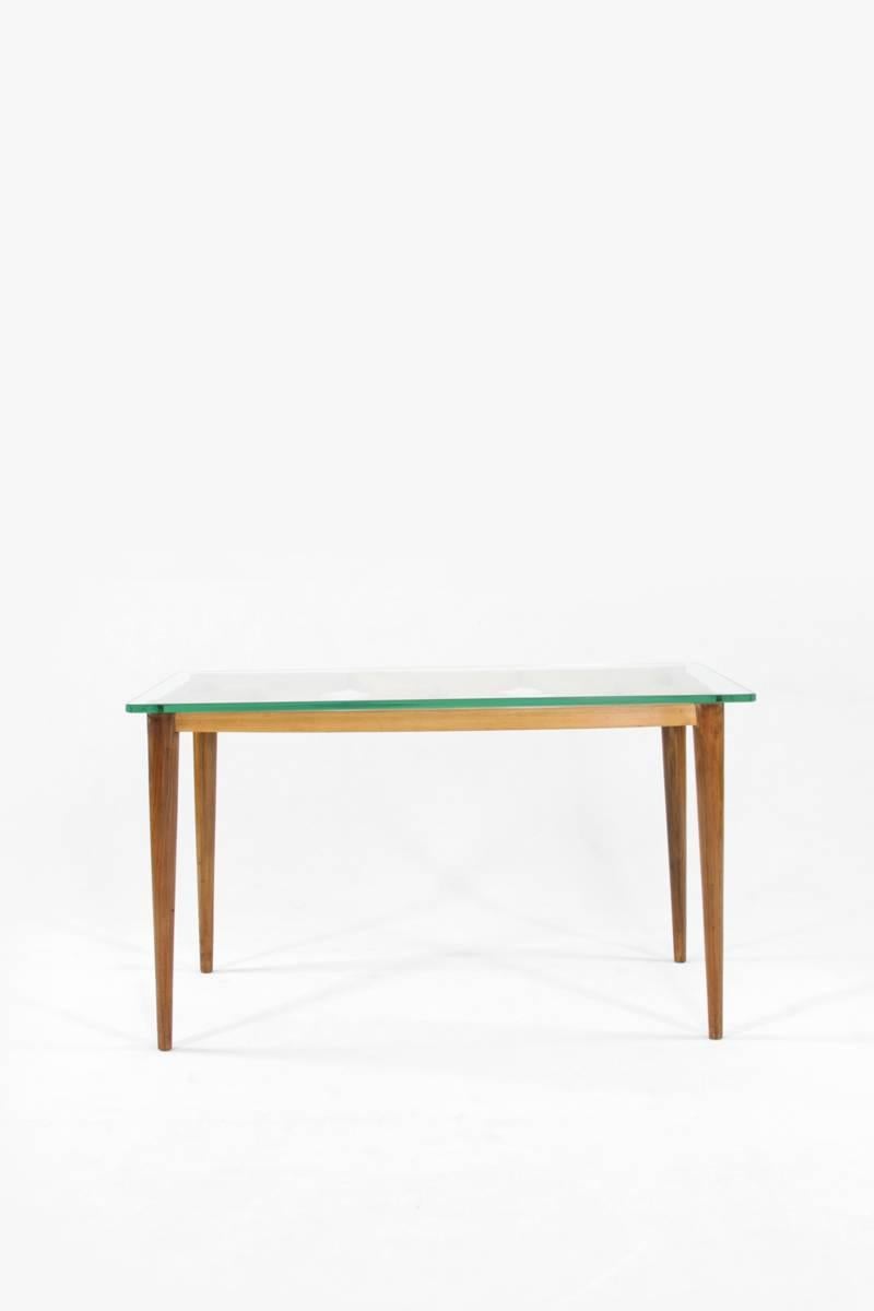 This coffee table in the style of Paolo Buffa was designed in Italy in the 1950s. It has a simple and minimalist design, and looks elegant thanks to the interplay of walnut and maple wood and glass. The crossed beams on the frame serve as a