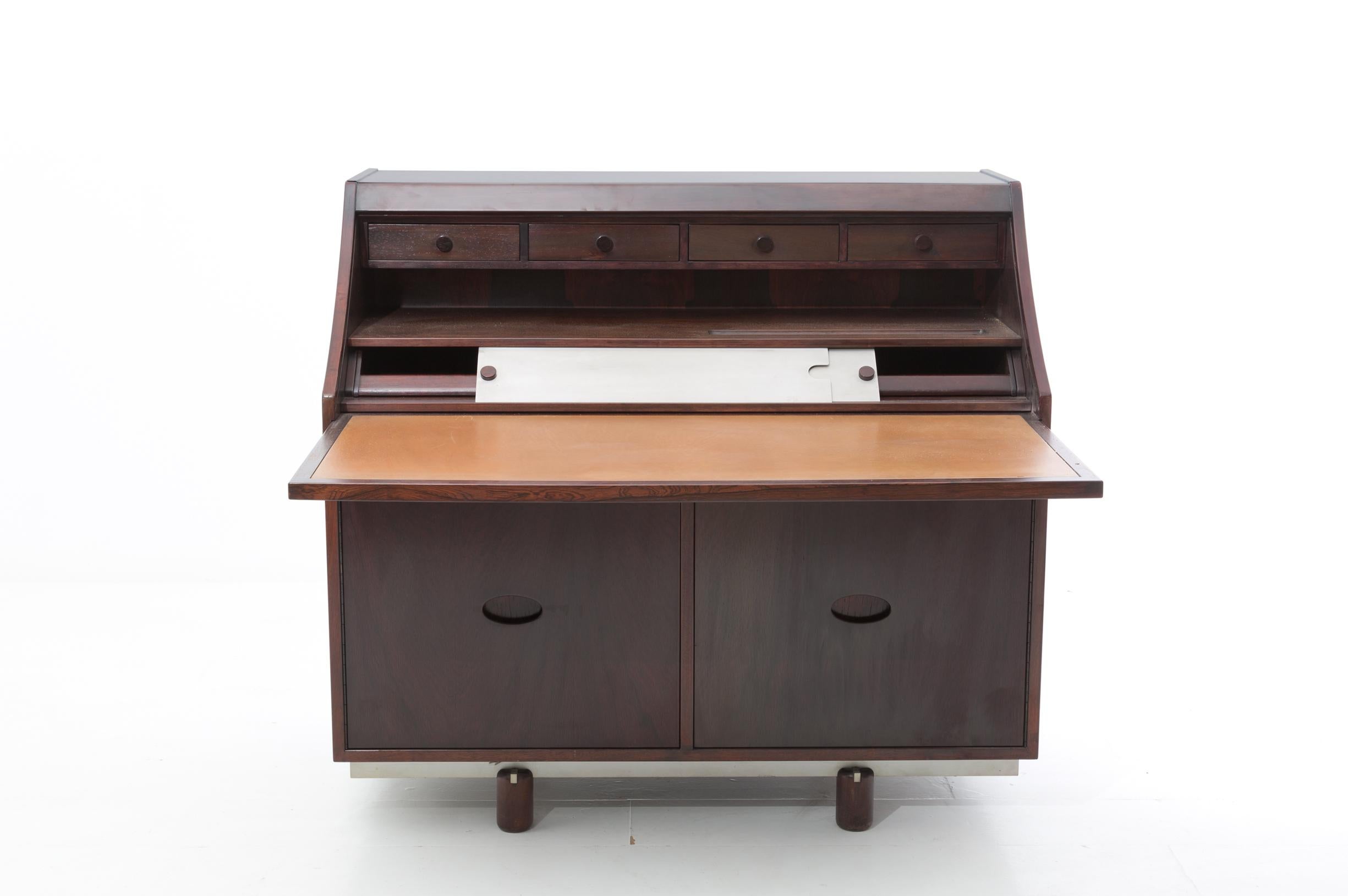 Writing desk designed by Gianfranco Frattini for the Bernini factory in 1960. The structure is in rosewood.
The desk is made of rosewood. The desk opens with a shutter opening. Inside there are 4 drawers for objects, a rosewood shelf and a white