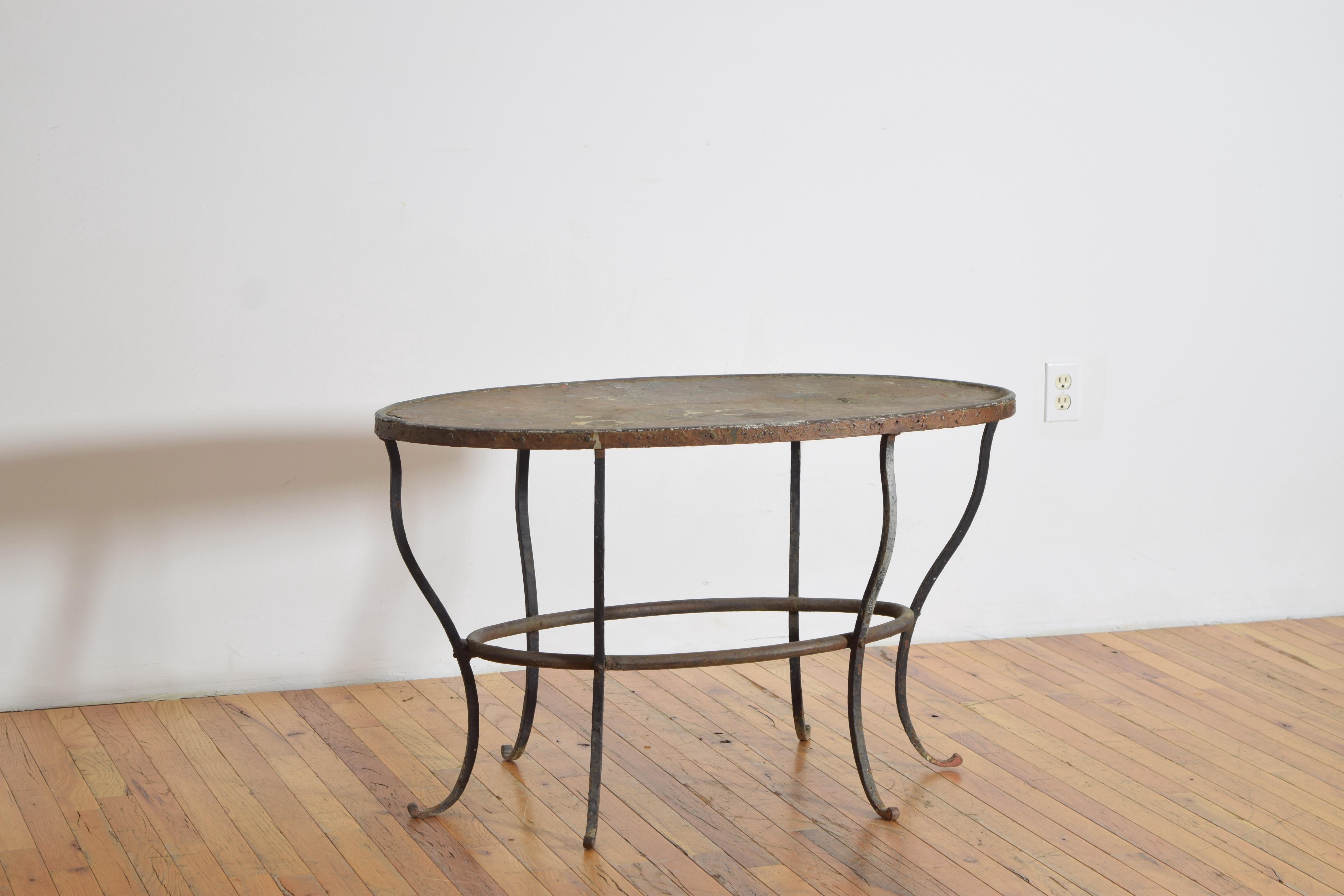 having an elliptically shaped copper top with varying degrees of distress atop an wrought iron frame joined by an elliptically shaped stretcher with curling legs