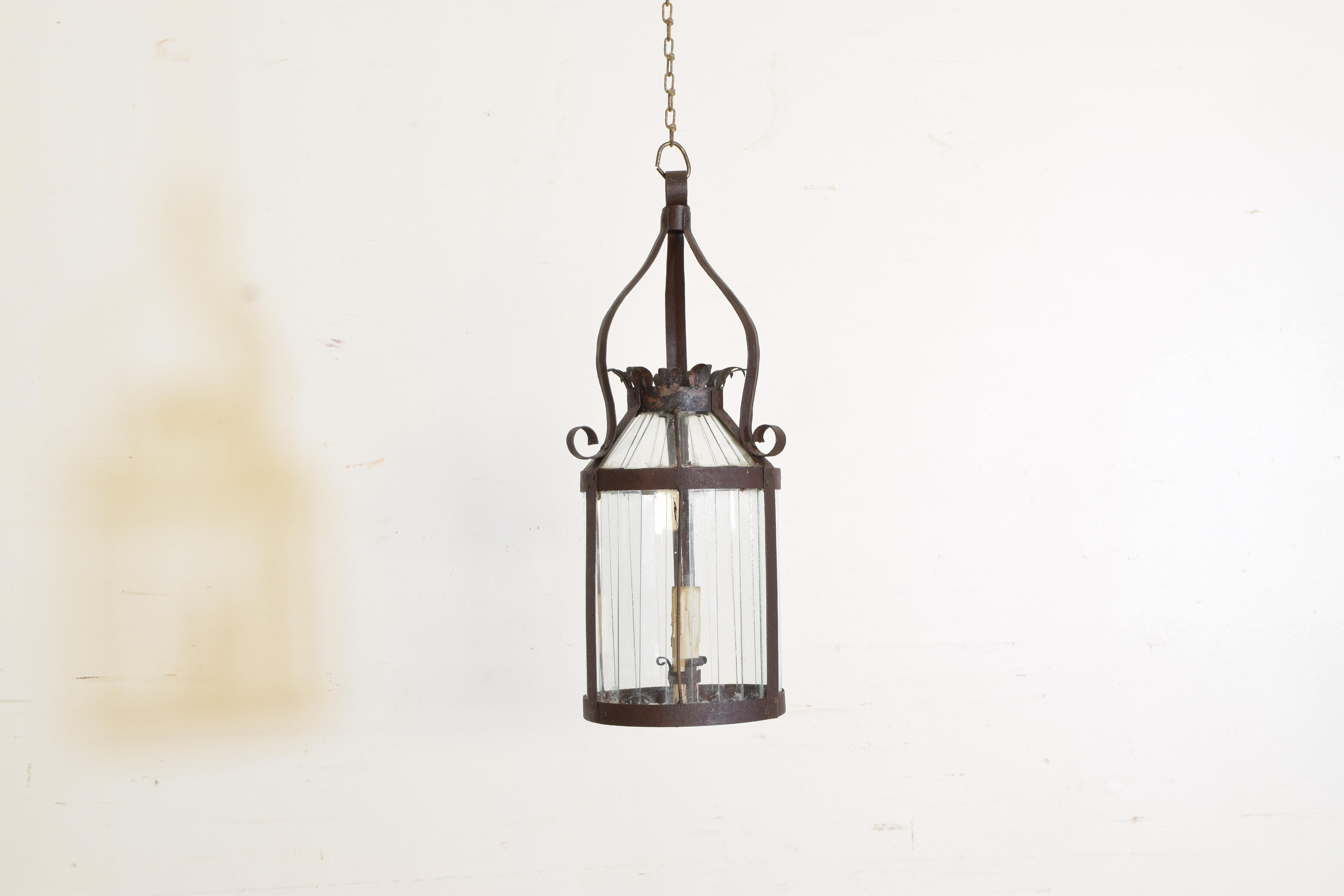 Hanging from a loop issuing three curved arms, the circular lantern with a domed open top with flared edges, the bottom of the lantern with a crossbar supporting the lone candle, the interior of the lantern fitted with vertical glass panes, late