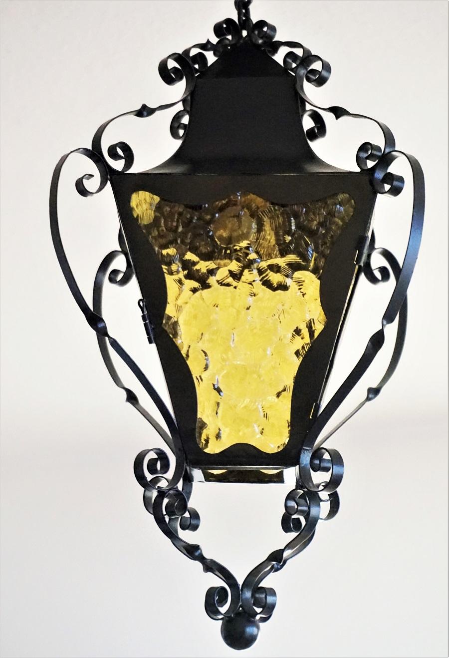 A four-sided Arts & Crafts wrought iron lantern with yellow glass panels for indoor and outdoor use, France, 1920-1930. Brass and porcelain E27 light socket for a large sized bulb up to 100watt. One side can be opened as a door for bulb change. In