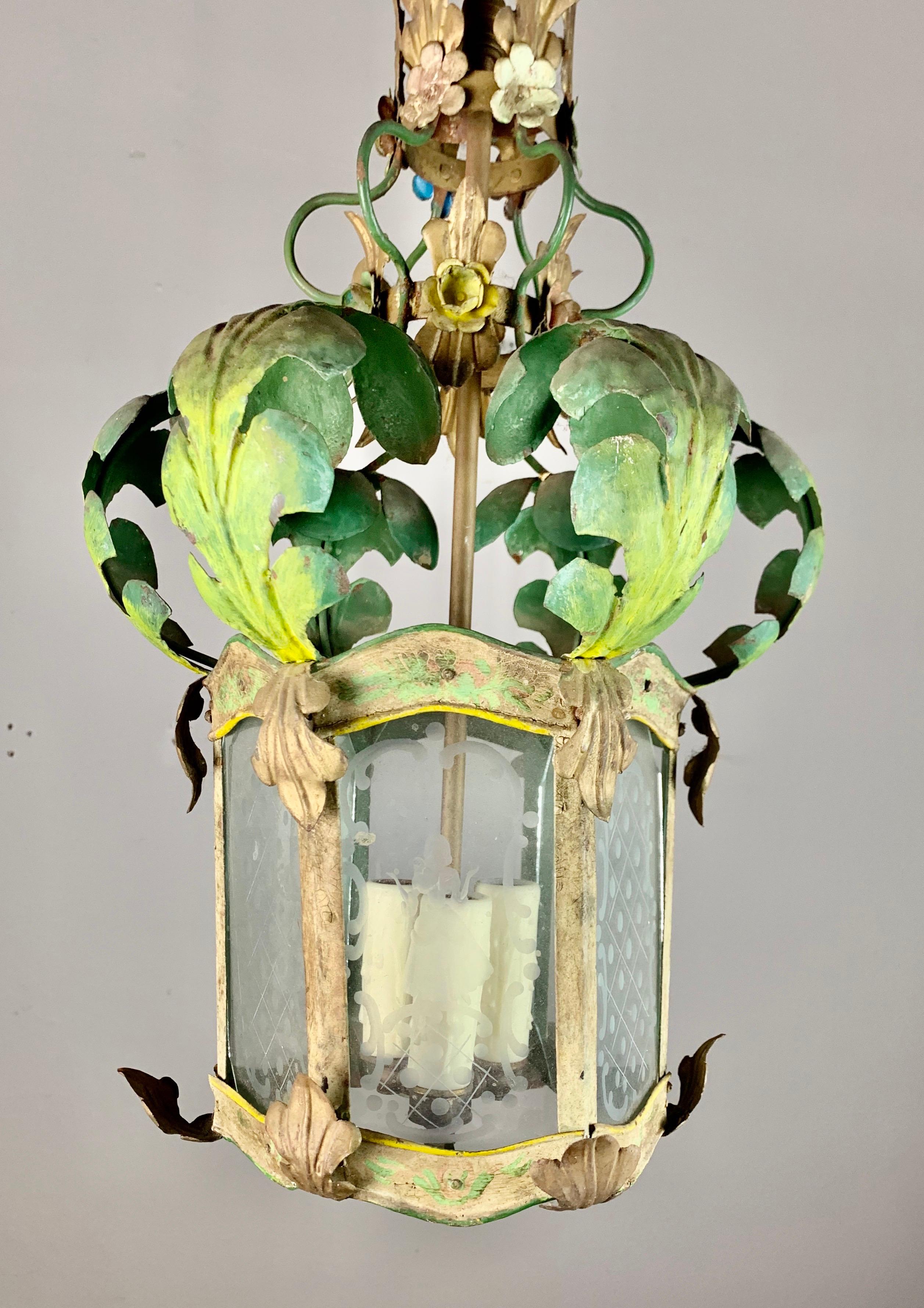 Italian wrought iron painted lantern with a gilt metal finish combined with a touch of vibrant green paint on the acanthus leaves for a pop of fabulous color. This lantern has beautiful fine etched glass depicting both a man and woman on opposite