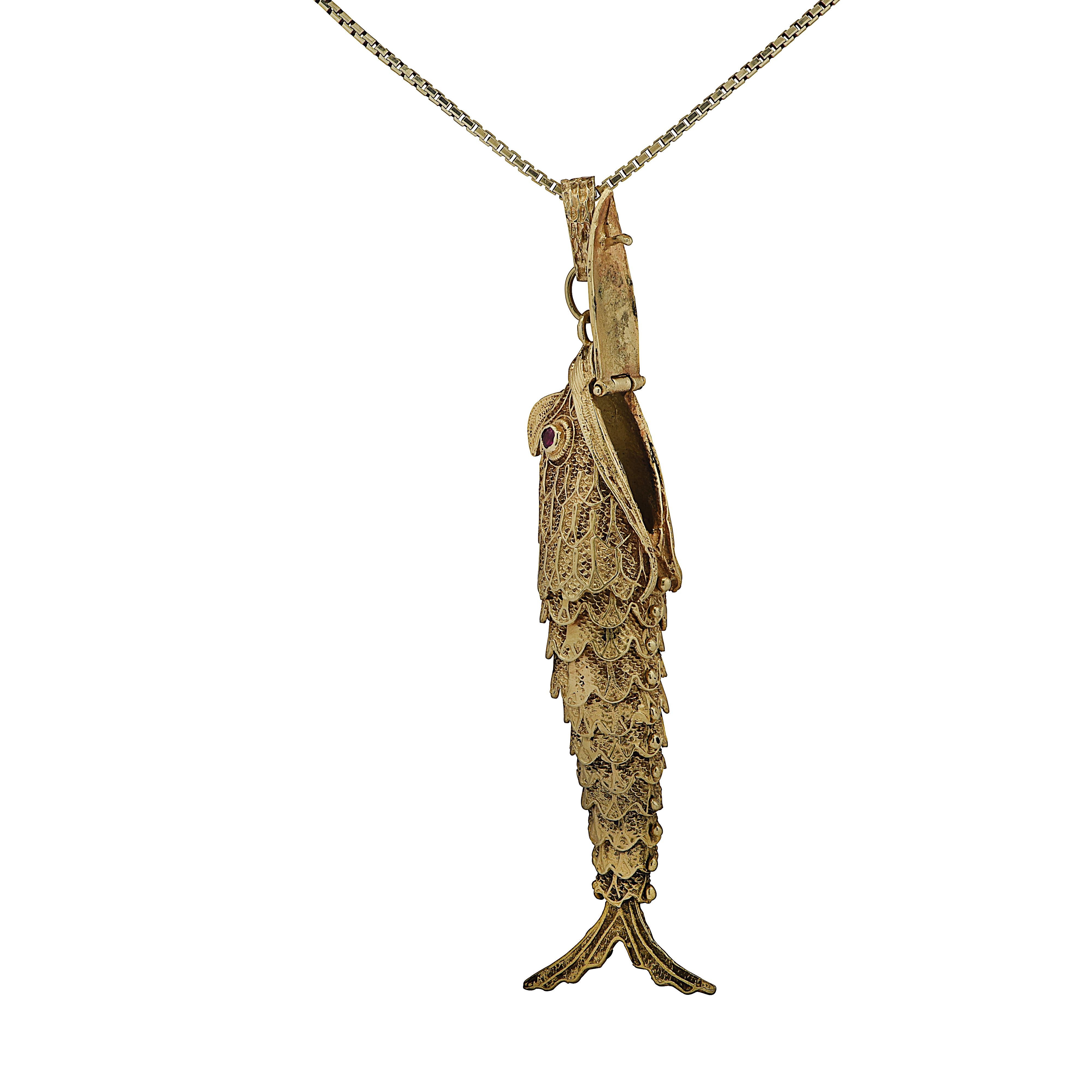 Stunning fish pendant crafted in Italy in yellow gold with two ruby red eyes. The articulated scales enable the fish to wriggle with movement. The hinged mouth opens to reveal a secret storage compartment. This pendant measures 3.5 inches in length