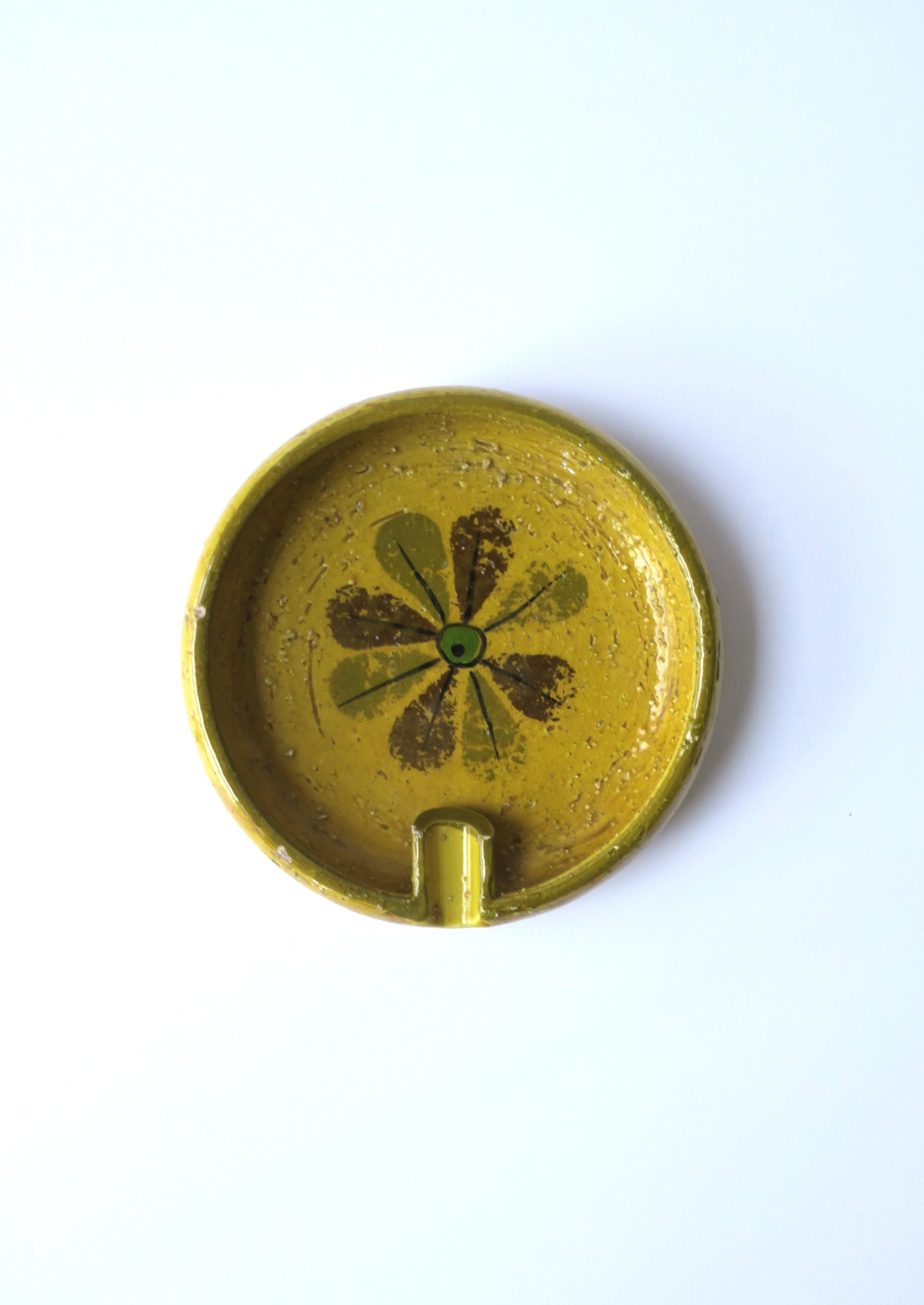 An Italian yellow pottery ashtray with flower center and lip for cigarette, Mid-Century Modern Italian period, circa mid-20th century, Italy. Pottery ashtray is yellow with flower design and an emerald green center. Piece is also being shown as a
