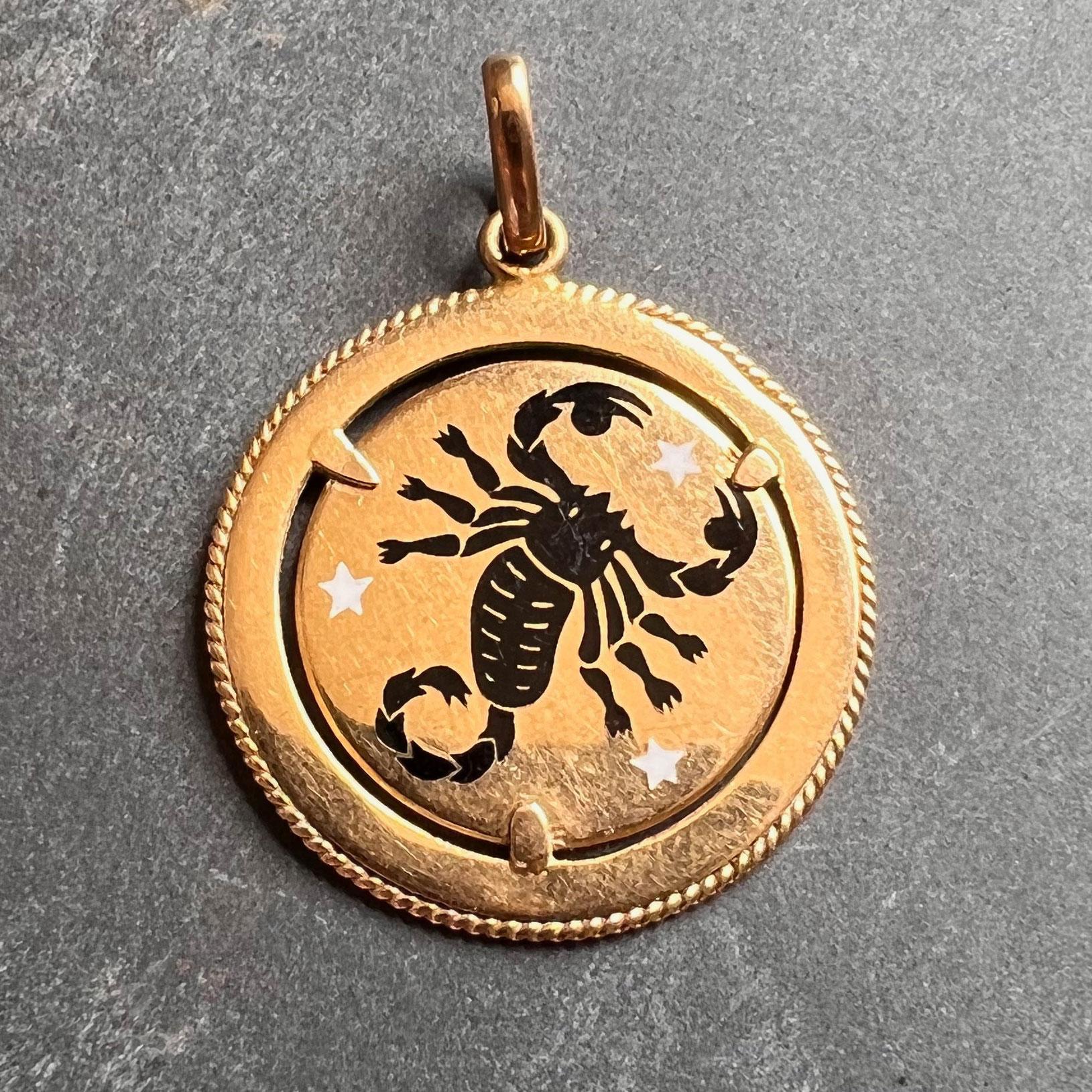 An 18 karat (18K) yellow gold charm pendant designed as a circular disc with an enamel depiction of a scorpion representing the zodiac starsign of Scorpio in a field of three white enamel stars. Stamped with Italian marks and 750 for 18 karat