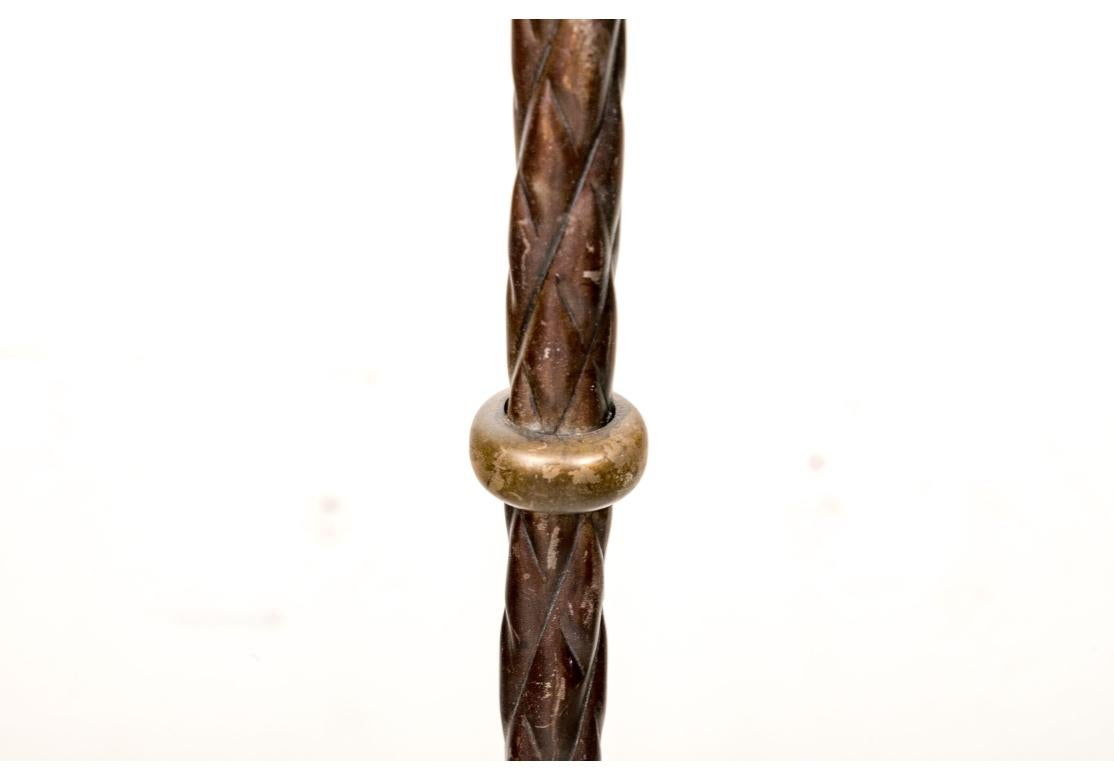 Ce lampadaire décoratif est doté d'un pied en métal torsadé patiné, d'un anneau en laiton et d'une coupelle en métal doré ajourée et feuillue au sommet. La base est un trépied à jambes incurvées et dorées, avec des brancards incurvés patinés et une