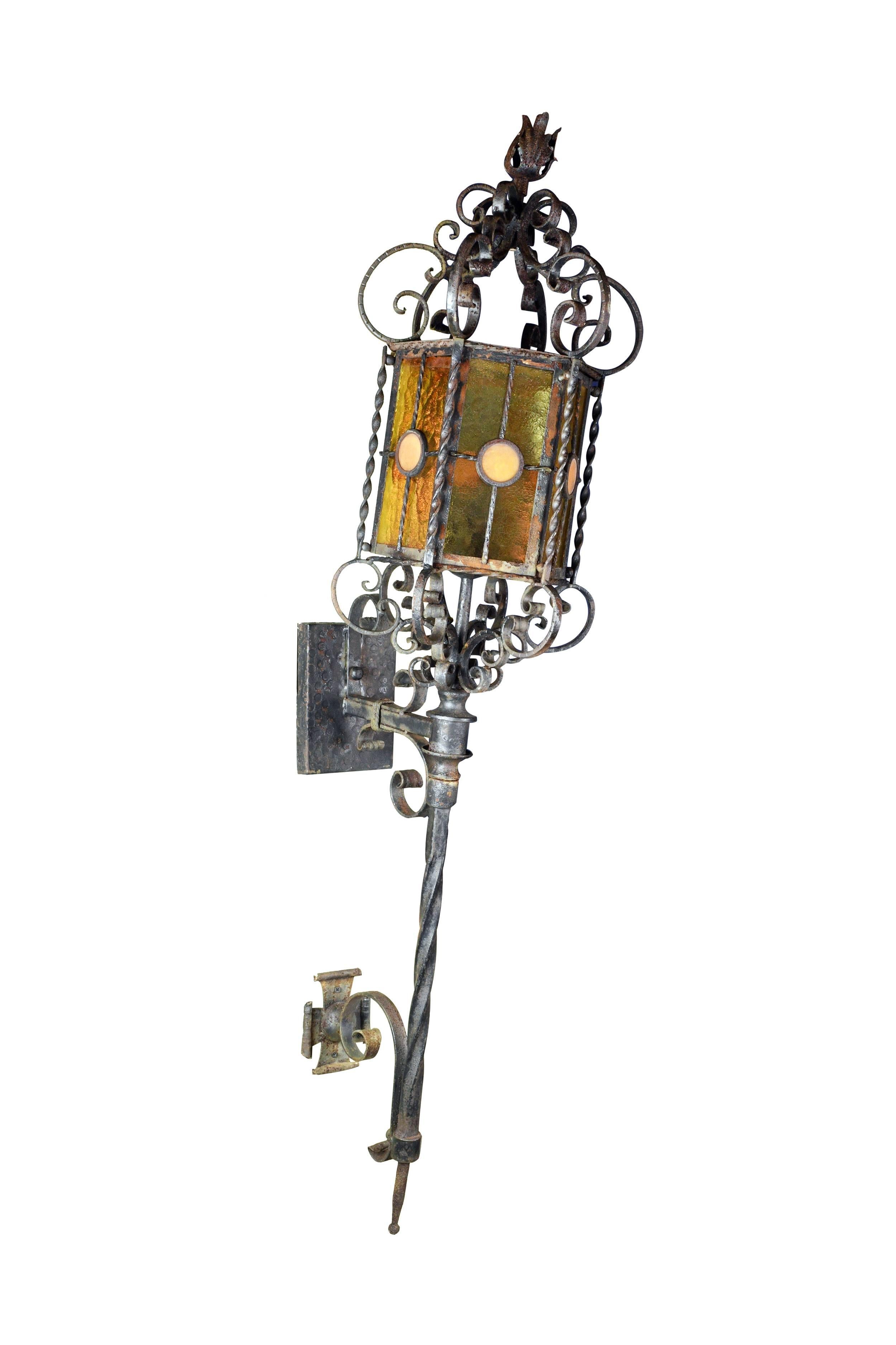 This large-scale exterior Italianate iron lantern sconce is highly decorative with curving lines that flow throughout the fixture. The glass shade is warm in tone, which works well with the cool metal body. The fixture, rather than sitting