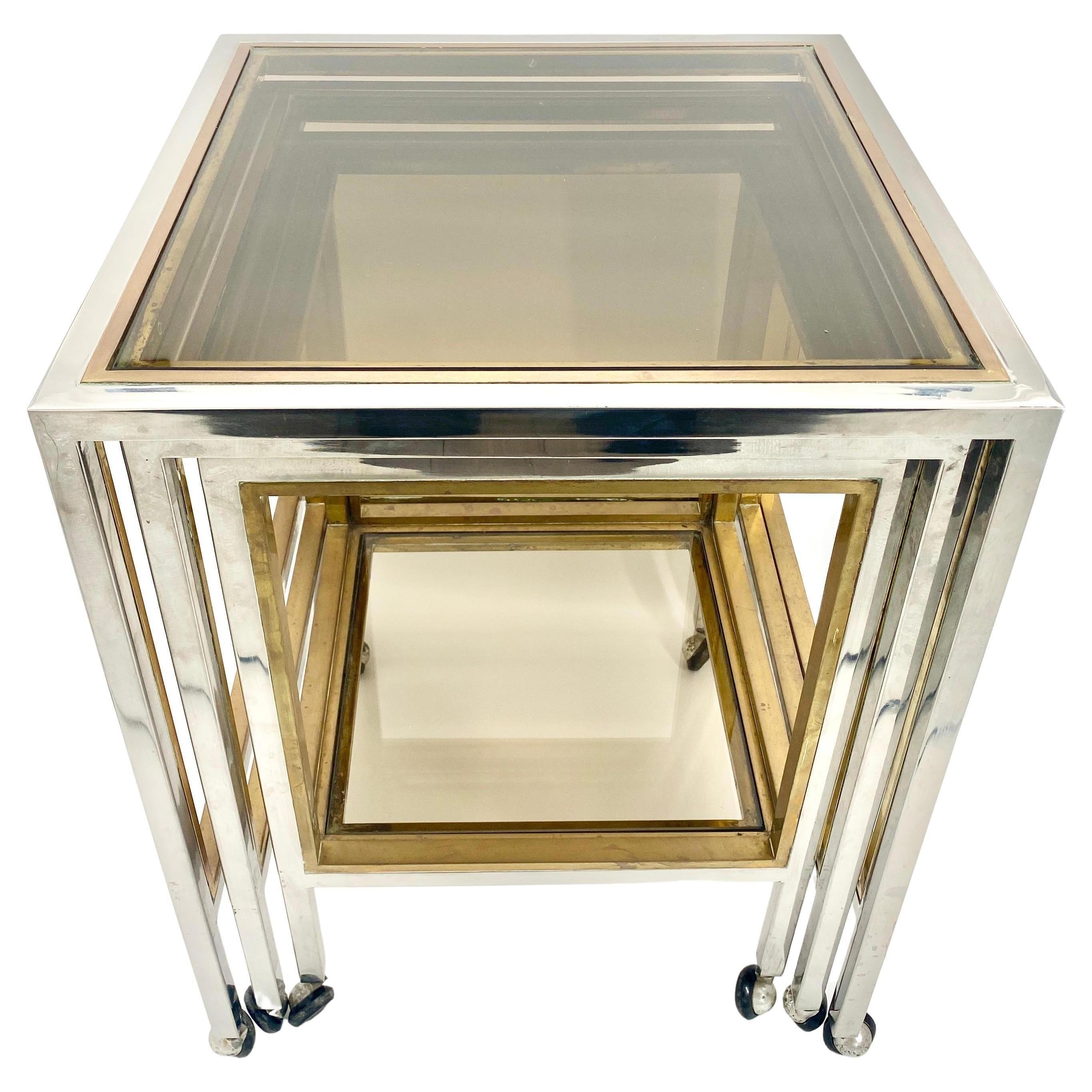 An original Romeo Rega Italian set of nesting tables on chrome, brass and smoked glass. The 3 tables are mounted on wheels with polished chrome frame that is edged in brass in the Hollywood Regency style. With the flexible design the 3 tables can be