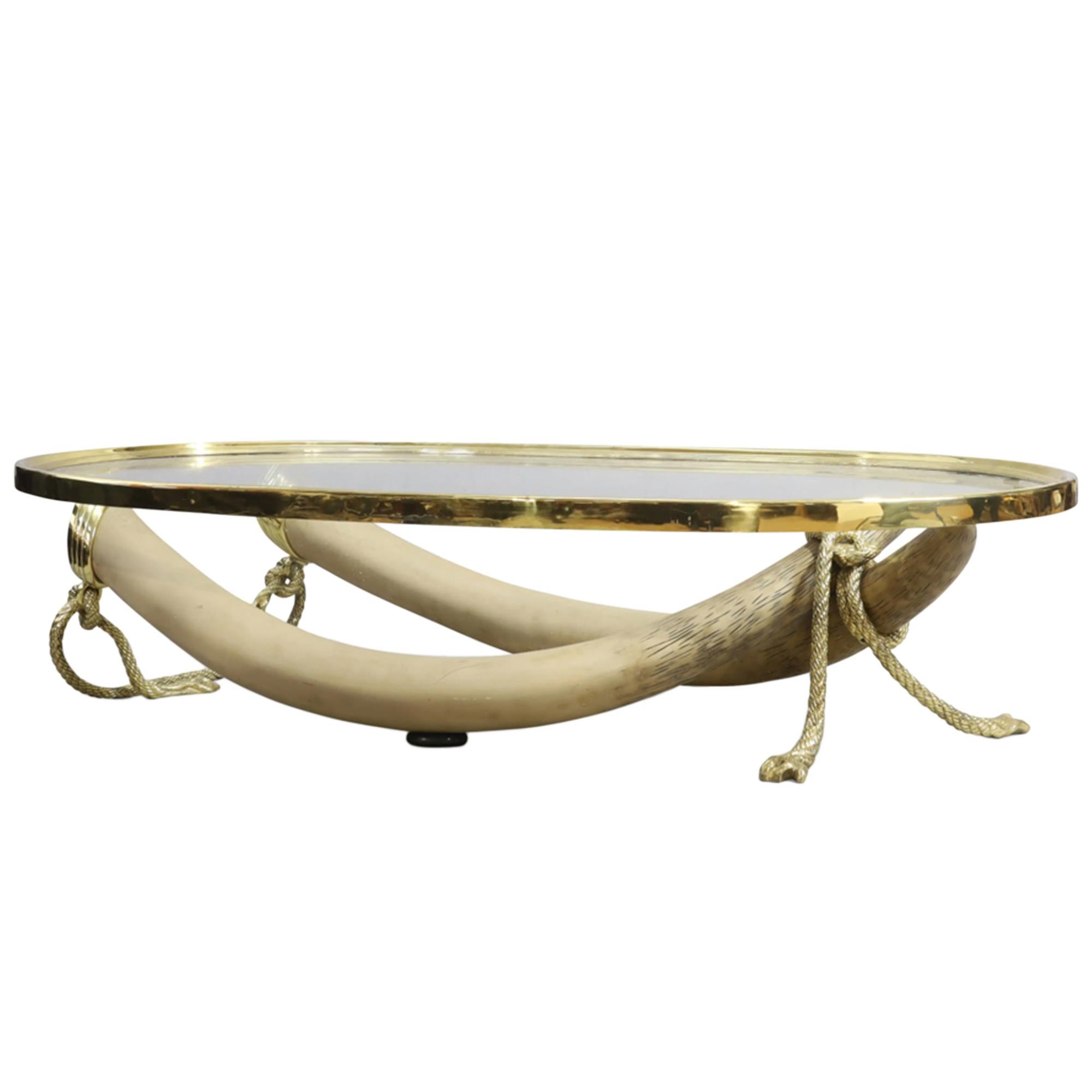 Une table basse de grande taille fabriquée par le luxueux fabricant de meubles espagnol Valenti. 

Le plateau rectangulaire en verre repose sur deux grandes fausses défenses en résine et des supports torsadés en corde de bronze doré. Le plateau de