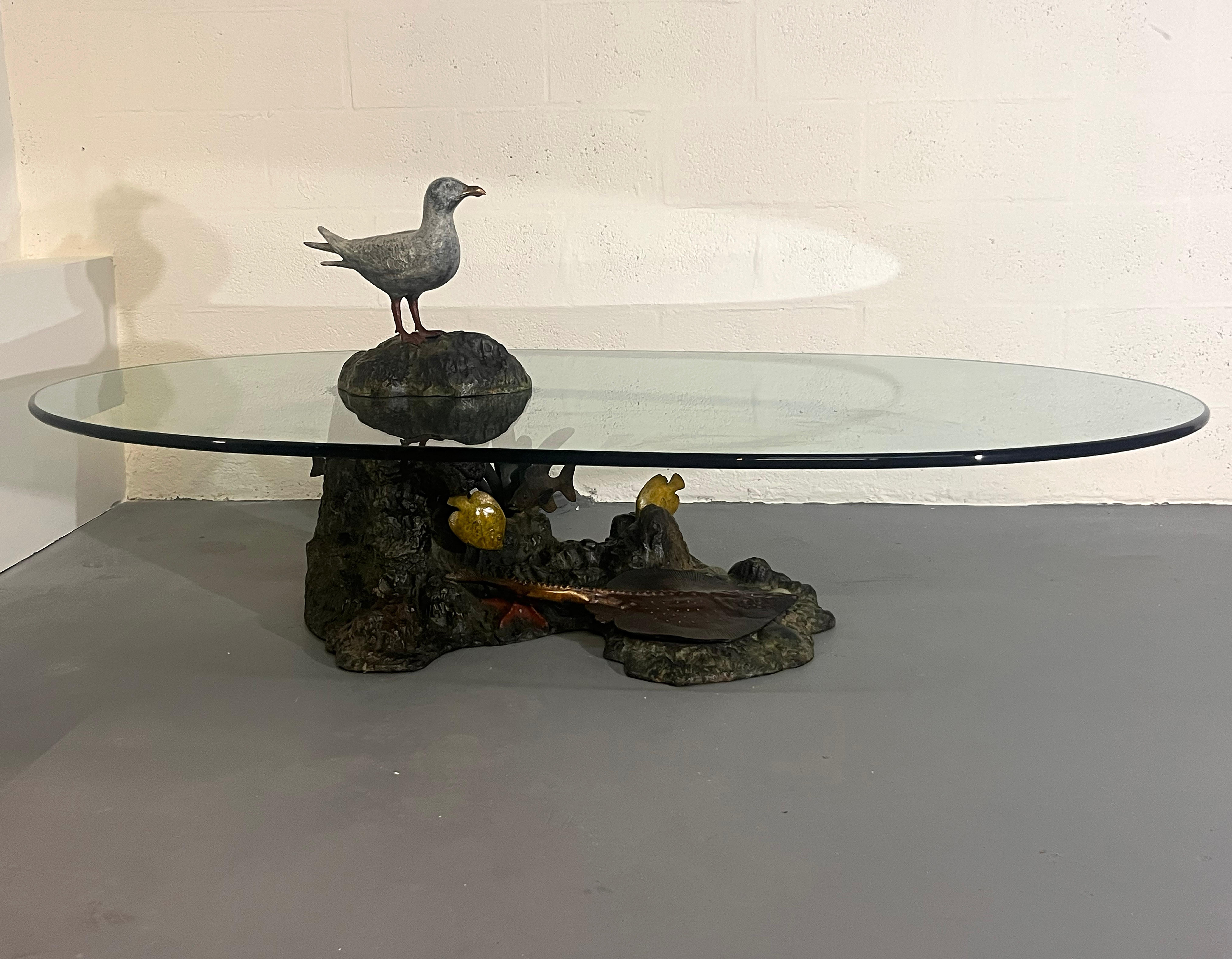 A striking sculptural coffee table by Valenti, Spain, circa 1970s.
The base is executed in gilt and patinated metal, beautifully modeled as a rocky seaside landscape with a perched seagull, fish, and underwater motifs in relief. The naturalistic