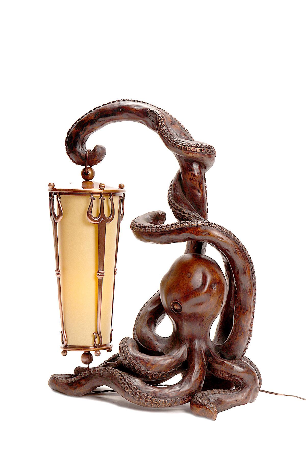 Art Nouveau desk lamp, made out of carved hazel nut wood, depicts an octopus holding a lantern with a tentacle. The lampshade is made of parchment encased by three tridents, made out of copper-plated brass. The socket and switch are in Galalith.