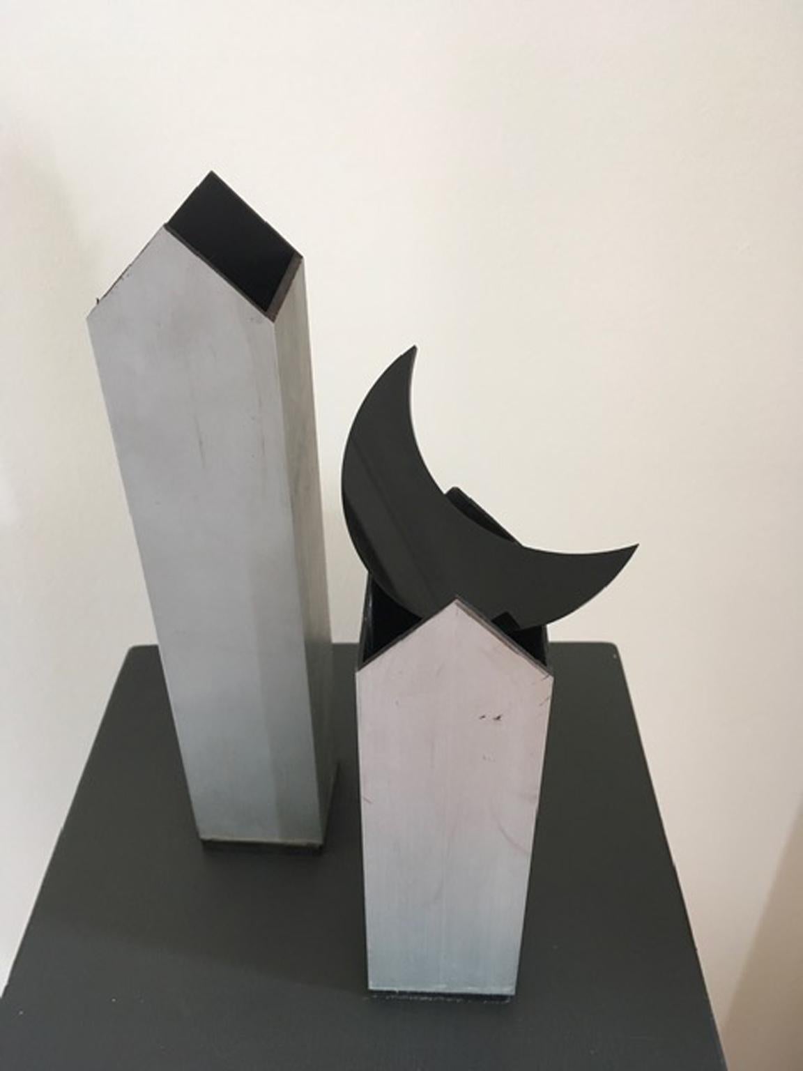 The twins in aluminium are a pair of metaphysical houses, the moon in black plexiglass is free and can be put on the top of one or other roof.
This sculpture means the freedom to create by yourselves and the choises how to be the same or to change