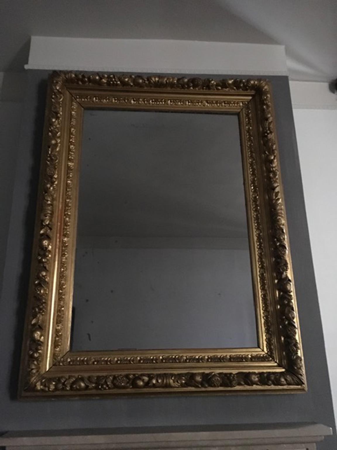 This a gorgeous mirrors in a golden wood frame with engraved fruits and flowers, full of details.
It is visible a red color, where the gold is fading, that is the basis color used in the past for the gold finish.
The fruit is the pomegranate, symbol
