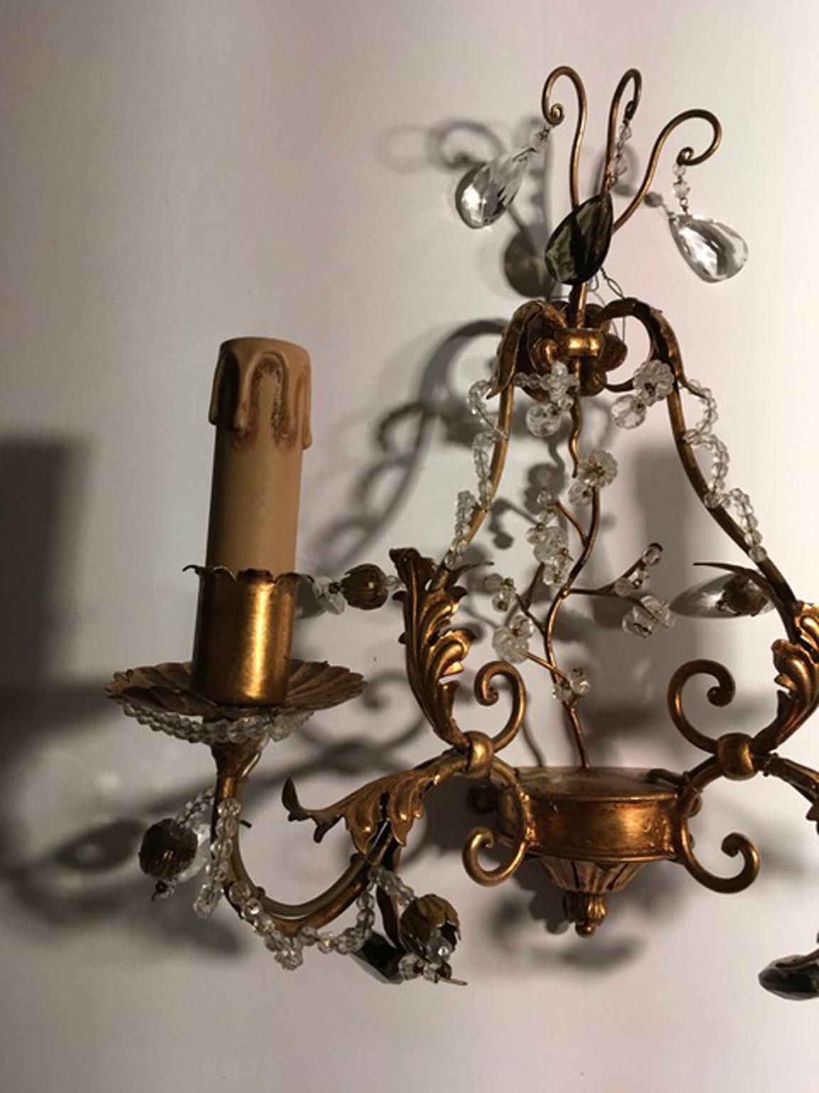 This is an Italian  patinated antique hand made iron wall sconce. The used gold finish is hand made. Many clear glass pendents and spheres enrich the wall sconce.
The two lights wall sconce is a contemporary handmade Italian production, made by one