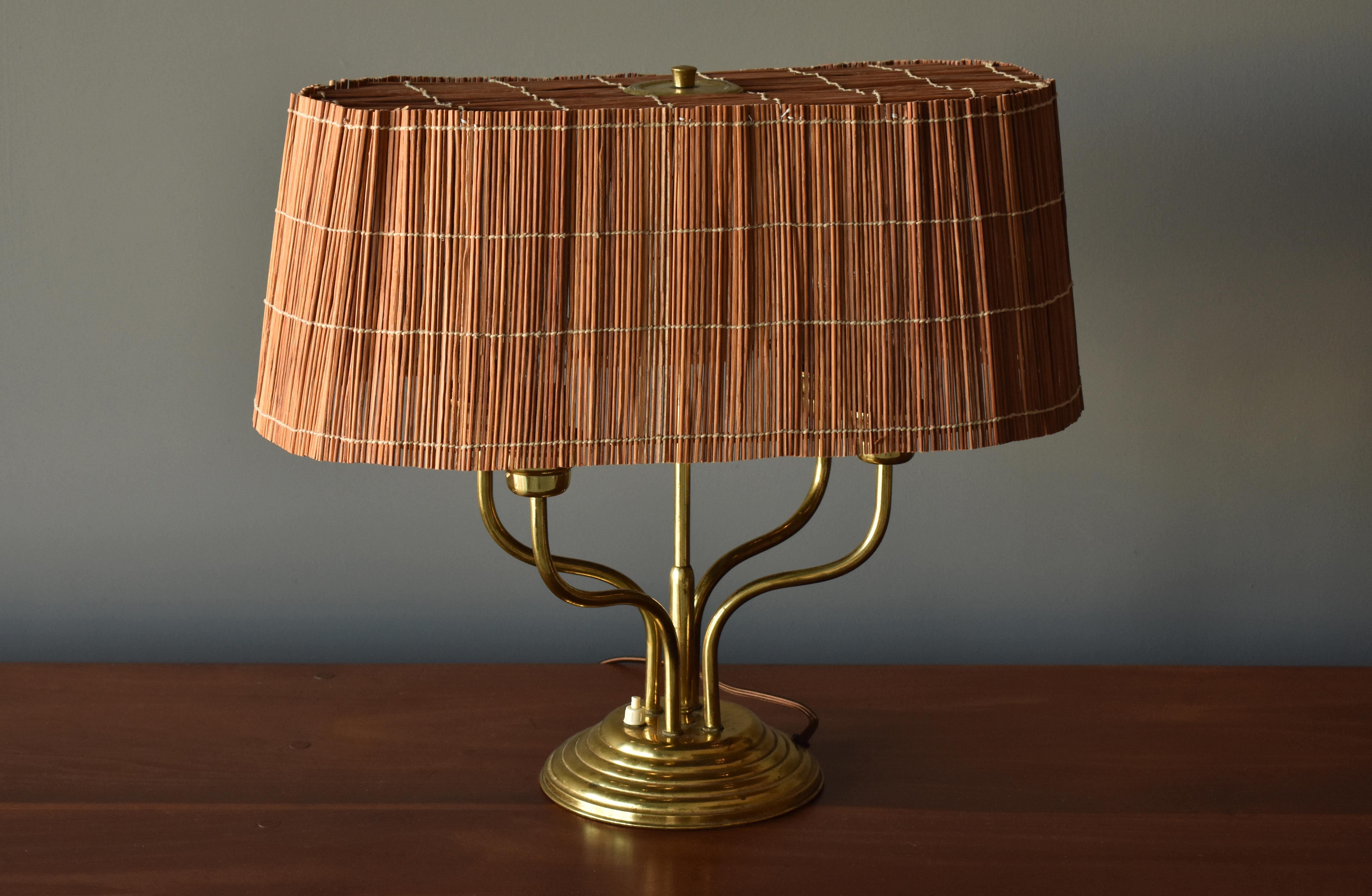 A rare and sizable table lamp by Finnish producer, Itsu. The ornate brass base features four-light sources mounted on organic arms. Warm and diffused light radiates through the large handmade reed screen. 

Model illustrated in manufacturers