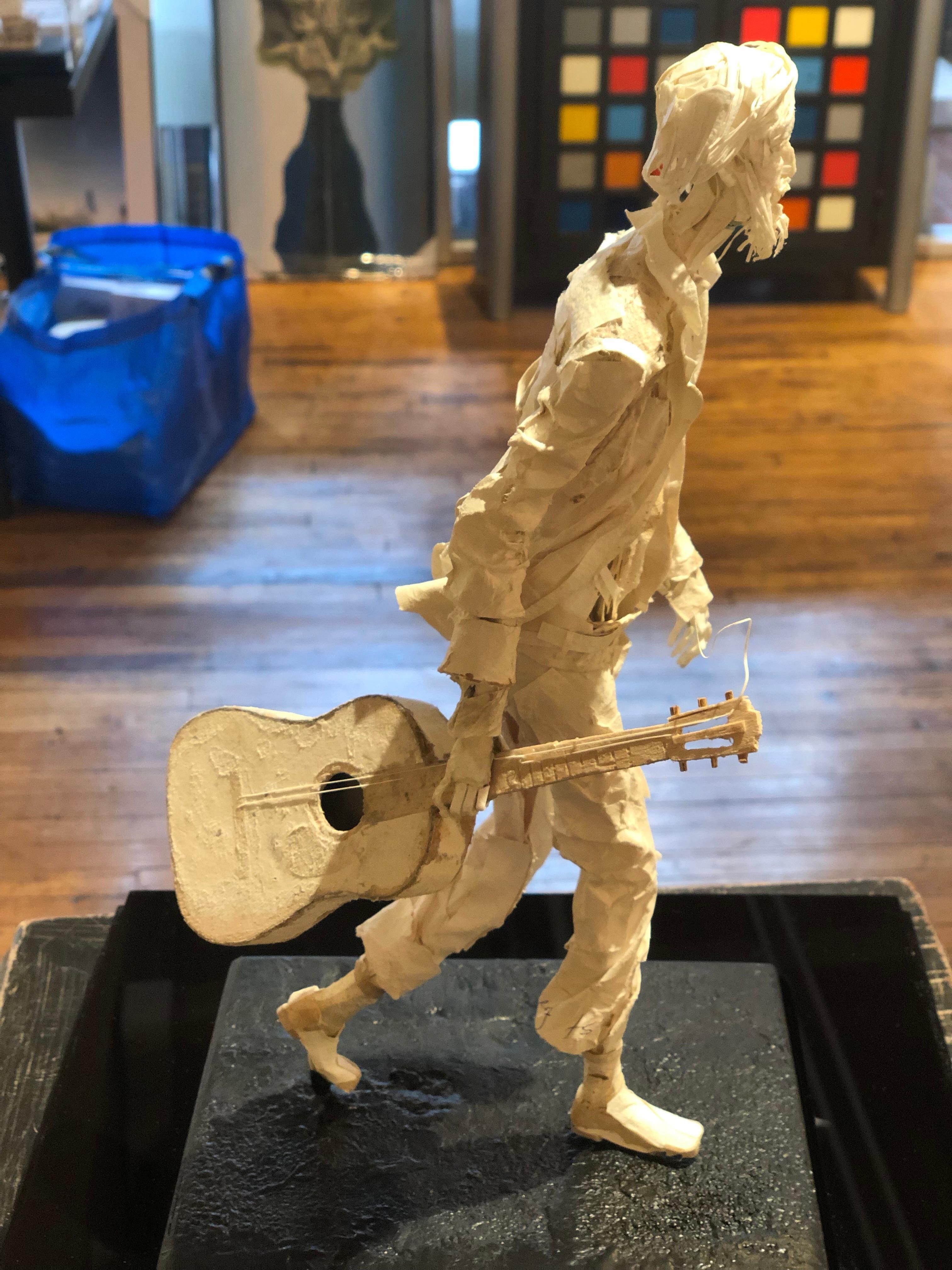 This realistic sculpture is created from scraps of paper and glue.  The sculpture is inspired by the characters found in cities around the world.  In this case, a street musician walks with his guitar.  The artist captures perfectly, the movement of