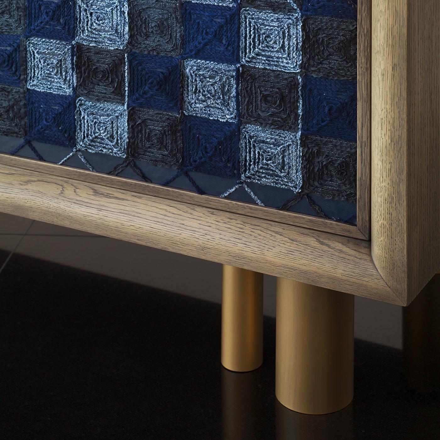 Handcrafted in oak, the Ivo blue cabinet stands proudly on six bronze legs and features a cool ash gray finish. In blue faux leather with checked embroidery, the cabinet opens to reveal three drawers and two glass shelves with a mirrored back for a