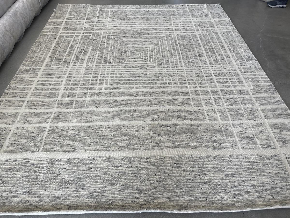 Blocks of low pile cut fibers form an intriguing geometric pattern in this contemporary wool area rug. Neutral ivory and charcoal complement a wide variety of color and wood tones. Hand made in India using vegetal dyes.