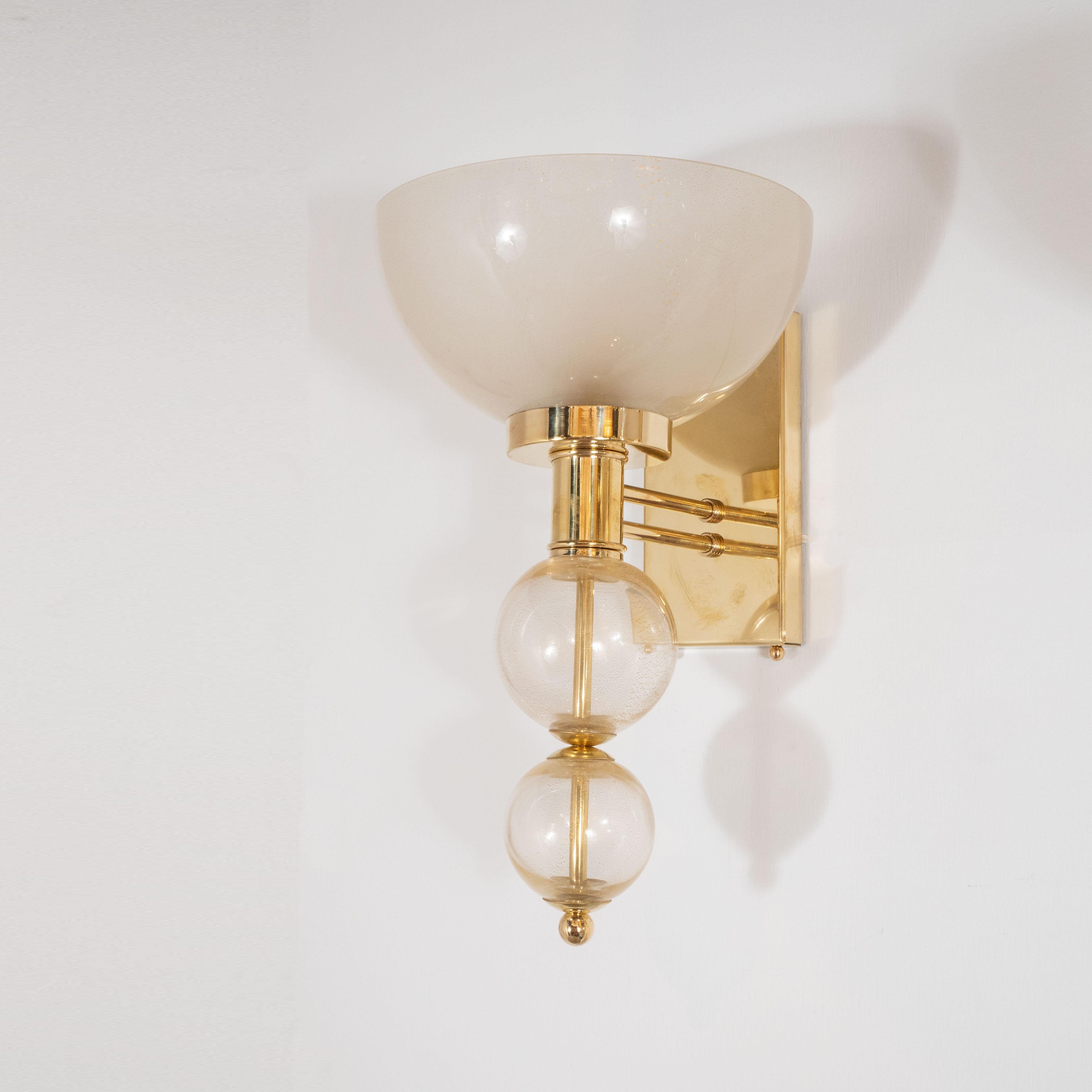 Pair of hand blown murano glass sconces consisting of an ivory glass cup sitting atop two gold spheres. Glass elements are separated by polished brass fittings. Sconces are suspended by brass rods and attach to wall by a brass wall plate. Wired for