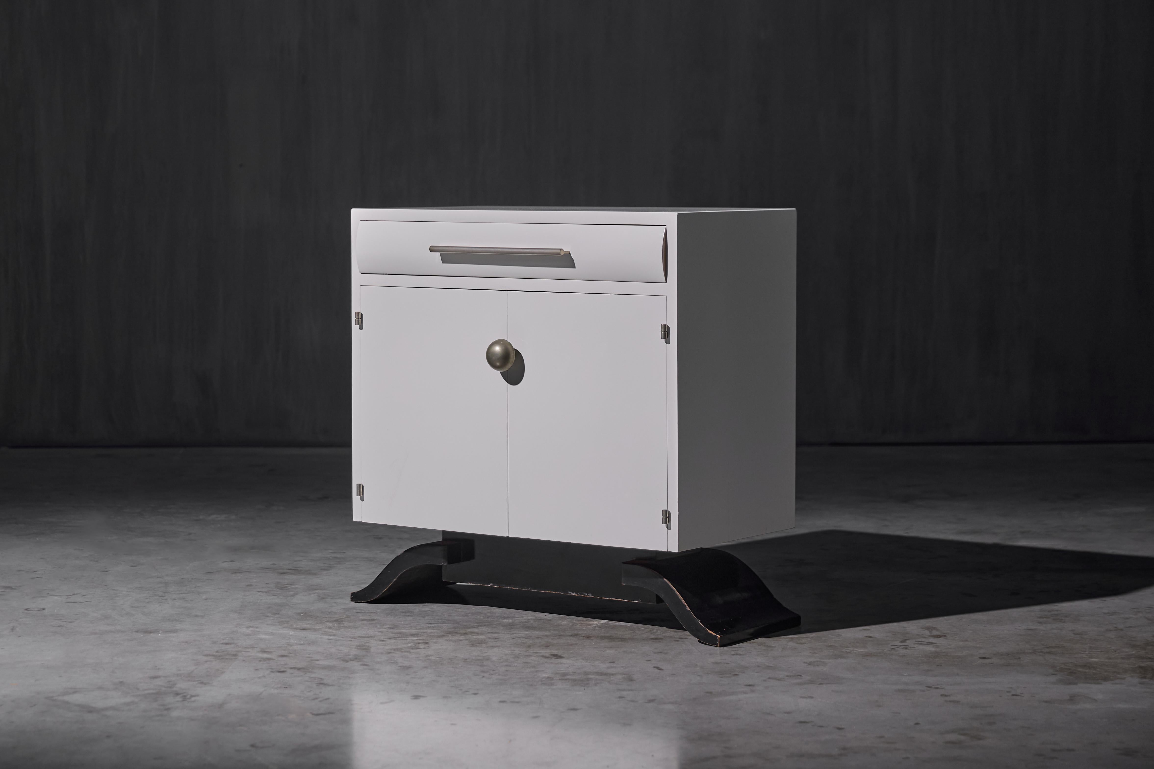 Realizzato in Belgio nel 1930, questo eccezionale mobile Art Déco fonde l'eleganza dell'epoca con un tocco di modernità. Le sue linee geometriche pulite contrastano con la base scultorea laccata di nero, la cui silhouette audace e ricurva accenna a