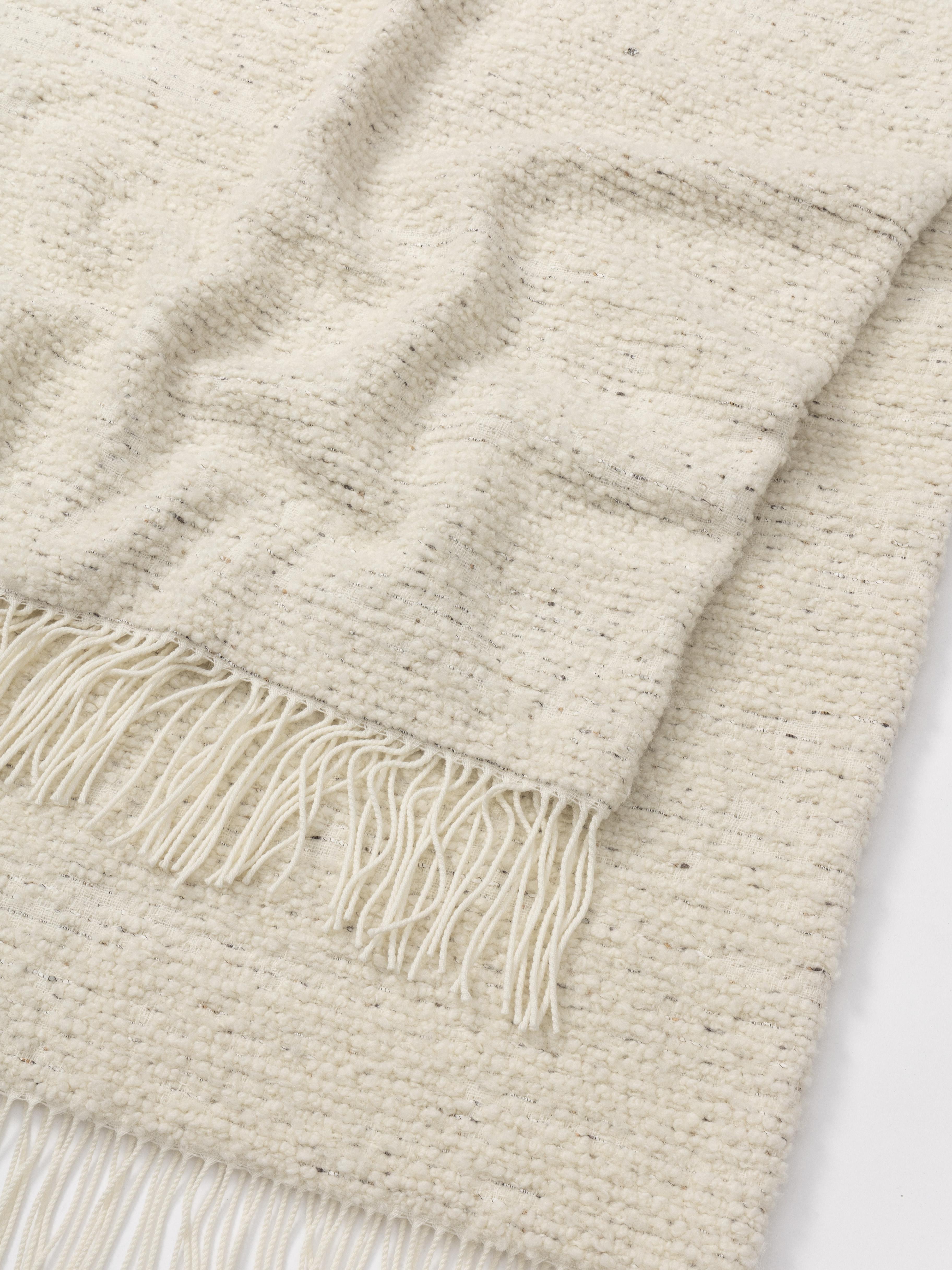 Plaid élégant et chaleureux, confectionné à partir d'un mélange haut de gamme de laine, de cachemire et de soie. Son tissage de style bouclé légèrement texturé, présenté dans un ton ivoire chaud, confère à cette pièce un caractère douillet et