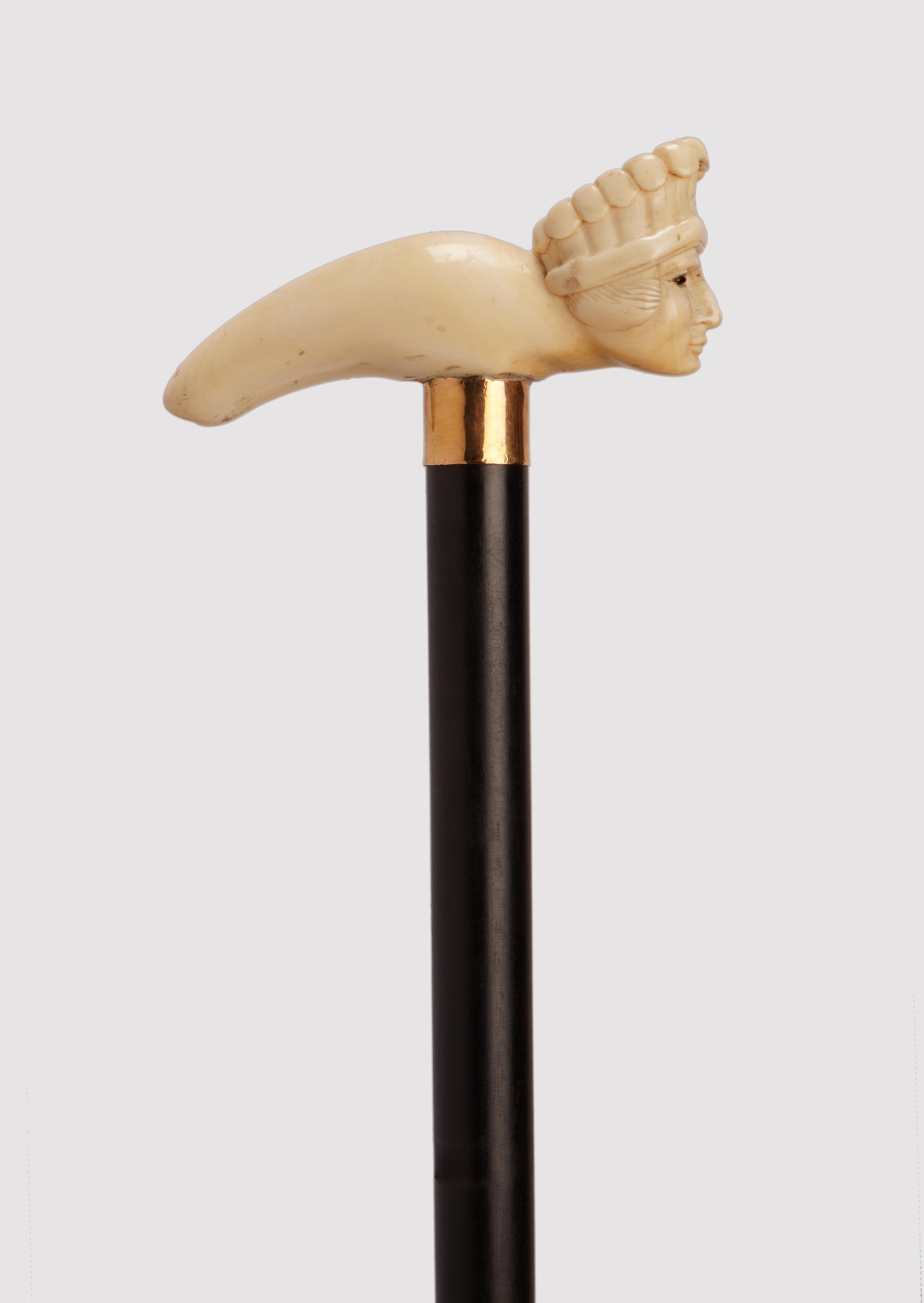 Bâton de marche :  Poignée sculptée en ivoire. La poignée est en forme de béquille, plane dans sa surface, avec la tête d'un chef amérindien central. Yeux en verre sulfurisé. Manche en bois d'ébène. Anneau en argent doré. Virole en ivoire.