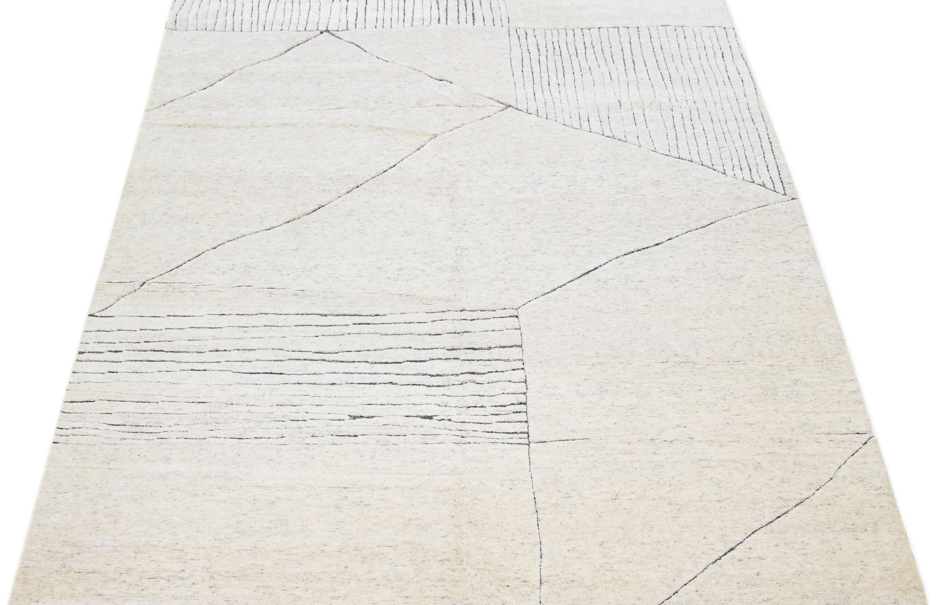 This luxurious wool rug features a timeless Moroccan pattern in a contemporary abstract minimalist style, utilizing ivory and gray tones to create a sleek and modern look. It is crafted using traditional hand-knotting techniques, ensuring