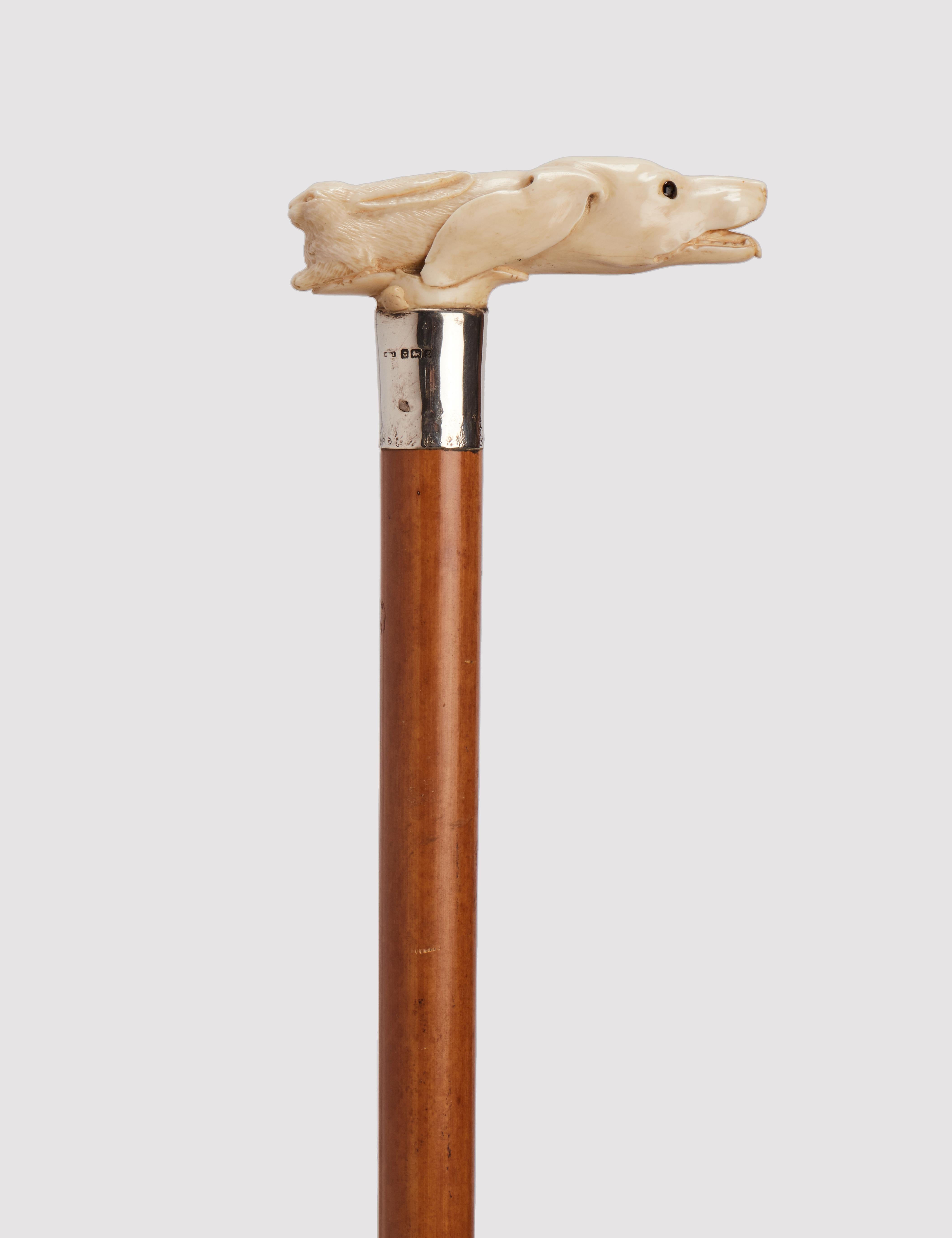 Walking stick: Ivory carved handle T shape, depicting an hunting dog head and a hare. Silver ring. Sulphur glass eyes. Malacca wood shaft. Metal ferule. UK  circa 1890. (SHIP TO EU ONLY)