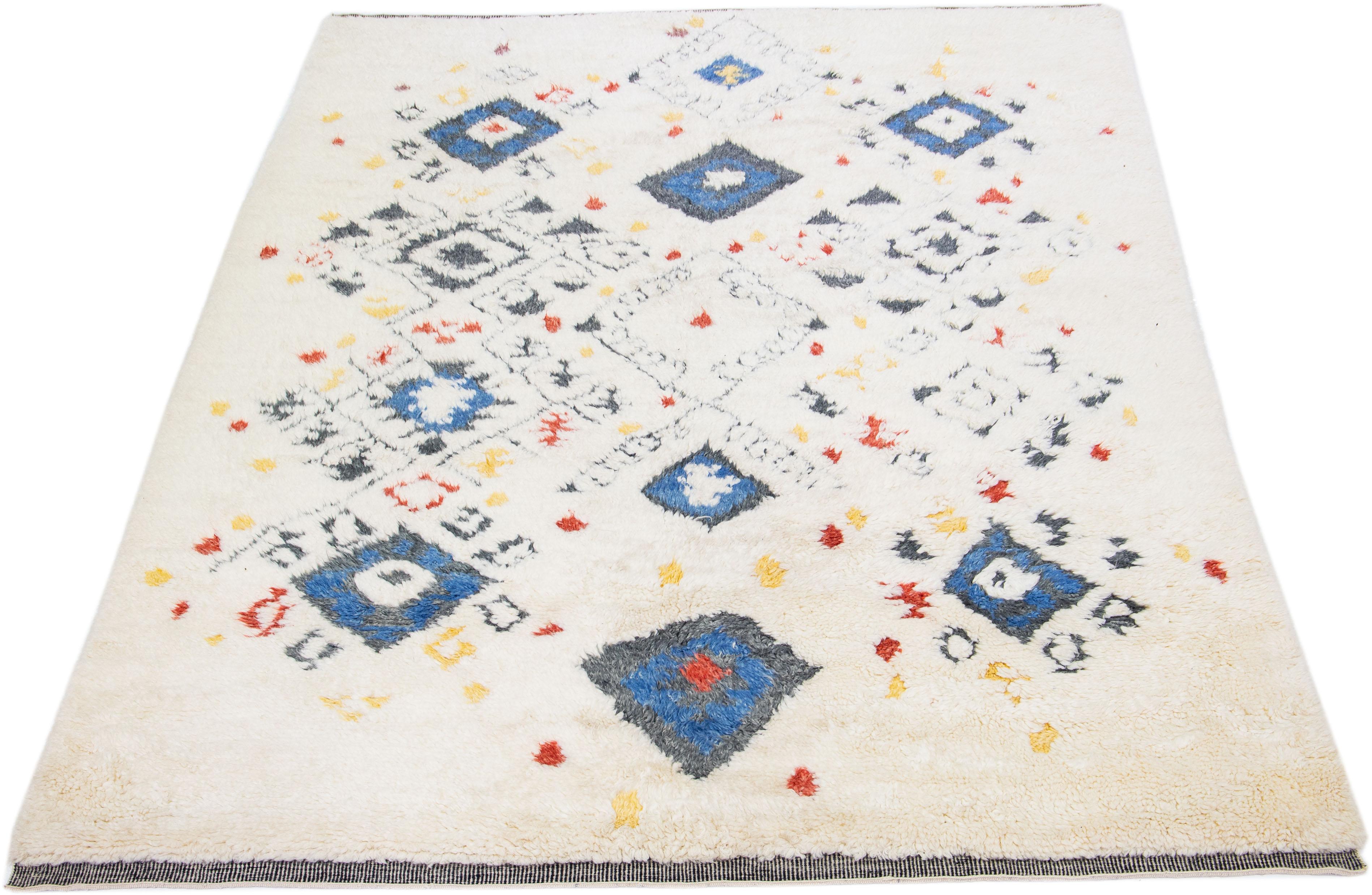 Beautiful Moroccan-style handmade wool rug with an Ivory color field. This Modern rug has gray, blue, yellow, and red accents featuring a gorgeous all-over geometric tribal design.

This rug measures: 9' x 12'.

Our rugs are professional