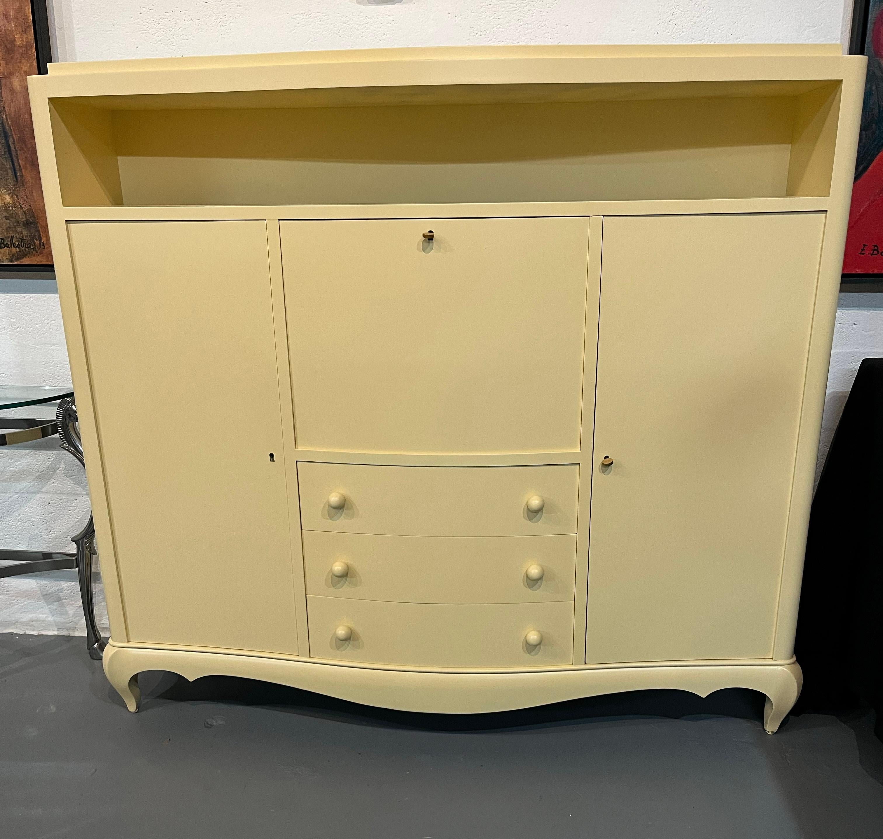 Very elegant and rare piece of furniture. This writing desk cabinet is in lacquered wood and has drawers and two side doors with shelves and bookcase compartments on the top. Refinished in precious ivory color lacquer.
The cabinet is standing on a