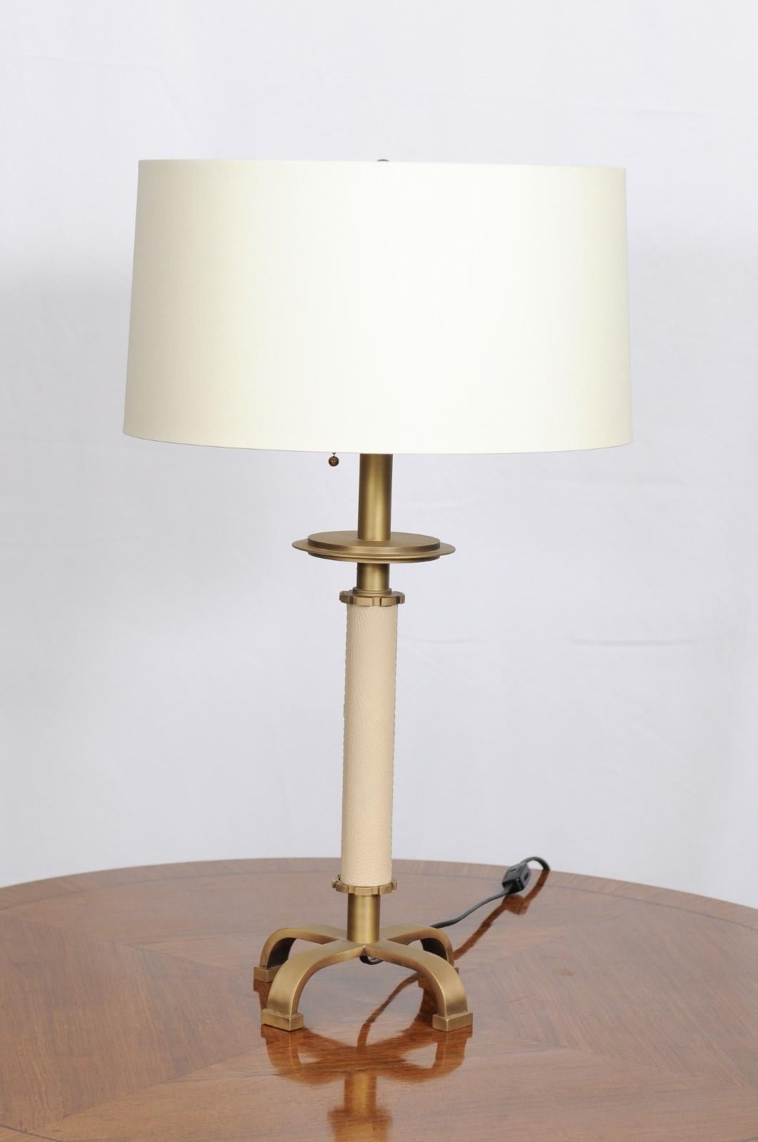 Ivory leather table lamp from the Thomas Pheasant Collection for Baker. An ivory leather column rests above four brushed brass legs for a sleek modern aesthetic.