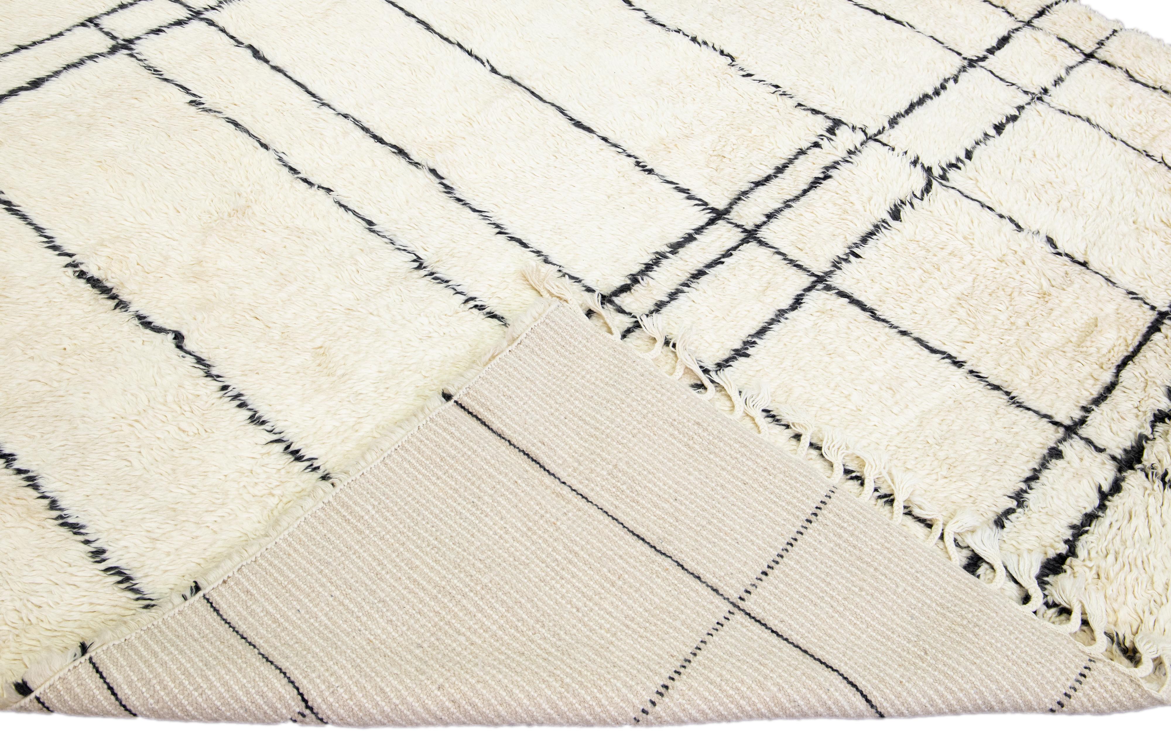 Magnifique tapis moderne de style marocain en laine nouée à la main avec un champ ivoire. Cette pièce présente des franges beiges et des accents géométriques noirs dans un magnifique motif all-over.

Ce tapis mesure : 8'2