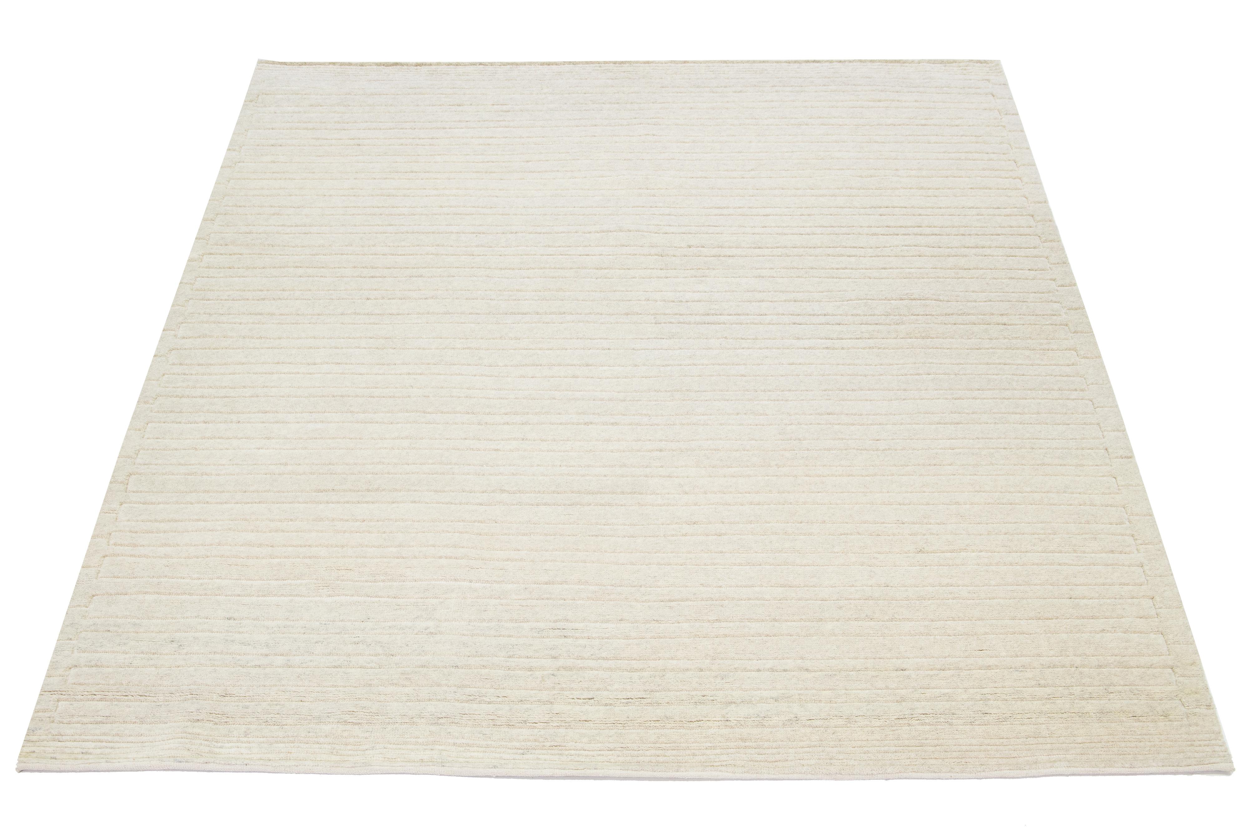 This hand-knotted rug, designed in a Moroccan style, is crafted from wool and exhibits a captivating minimalist aesthetic. It showcases contemporary stripes on a naturally hued ivory background.

This rug measures 8'3
