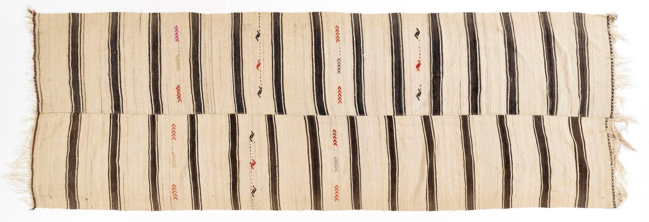 A beautiful and simple flat-woven runner from the 1960s is made of natural hand-spun wool in shades of brown and cream. It features a banded design with hook and fishbone motifs in places. It is in good condition with no issues, professionally