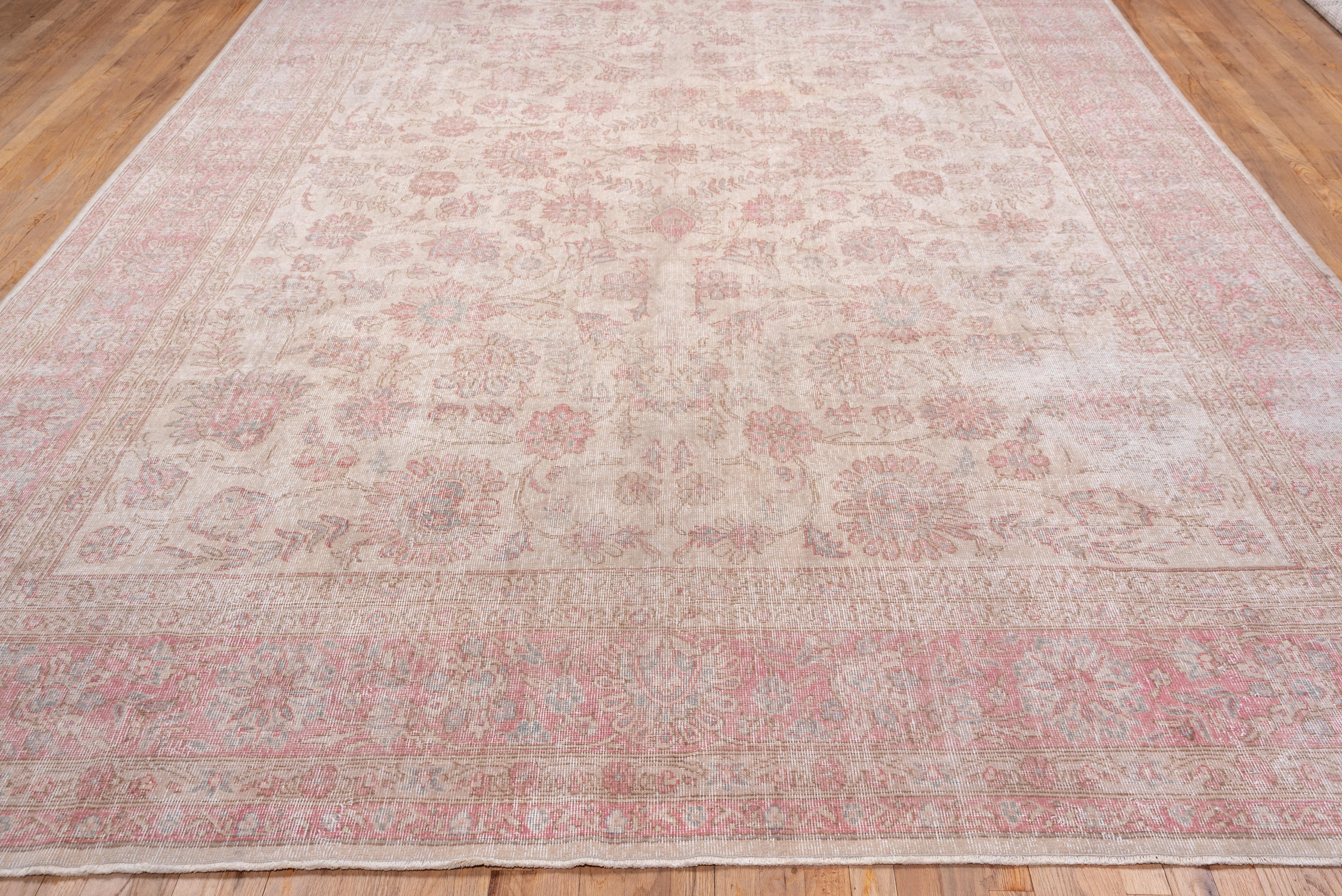This somewhat worn to nearly distressed carpet shows a cream field with an all-over petal rosette, leafy stem, vine and bud-palmette pattern detailed in tones of medium pink to light brown.