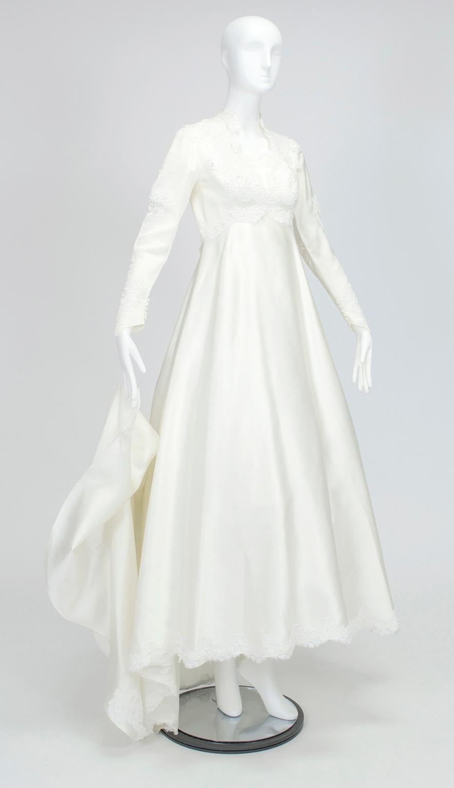 Cette robe de mariée à jupe complète, très traditionnelle et d'allure royale, couvre tous les aspects de la vie. Bien qu'elle dissimule les bras et le cou pour des raisons de bienséance, son encolure Reine Anne donne de l'allure grâce à son plongeon