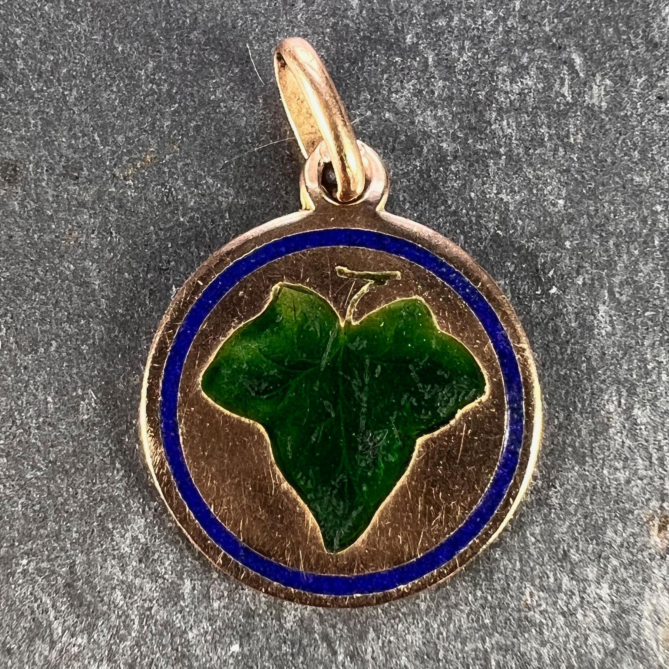 A 9 karat (9K) rose gold charm pendant designed as a disc depicting a green enamel ivy leaf surrounded by a blue enamel border. The ivy leaf represents fidelty and devotion. Stamped with a French import mark for 9 karat gold to the pendant loop,