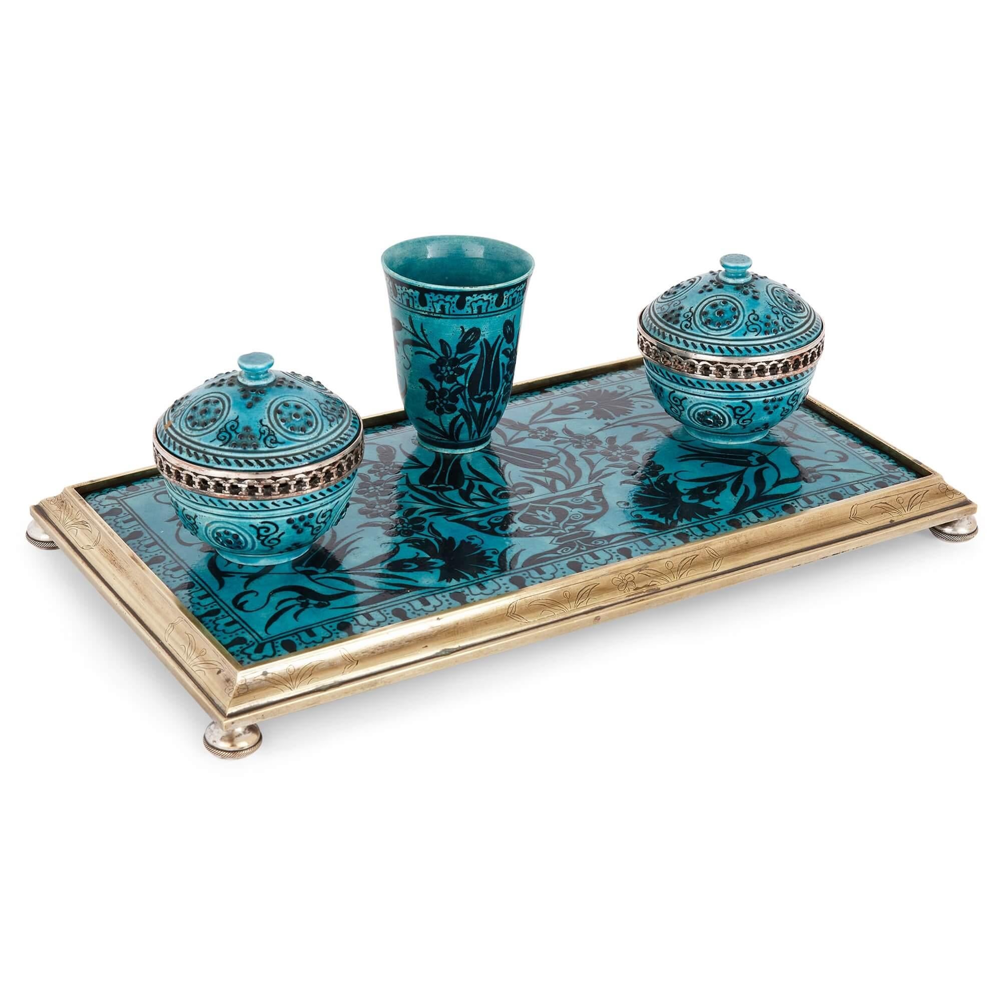 Iznik-style ceramic and brass-mounted ink stand
French, 19th Century
Height 10.5cm, width 34cm, depth 19cm

Revealing a vase and flowers contained in a border of repeating pattern-work, with two lidded inkwells flanking a central holder, this