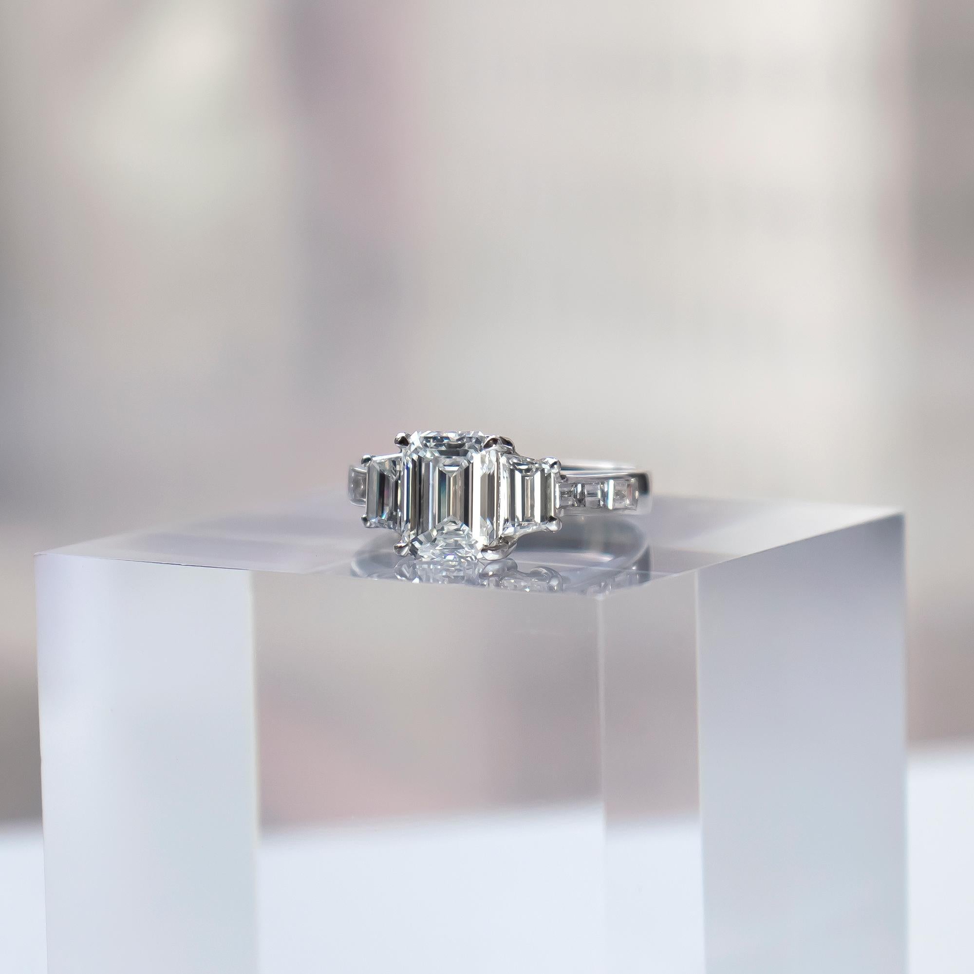 This handmade, three-stone ring recently acquired by the house of J. Birnbach features a natural, certified 1.61 carat emerald cut diamond of F color and VS2 clarity as described by GIA grading report # 1378269503. Flanked by a pair of beautifully
