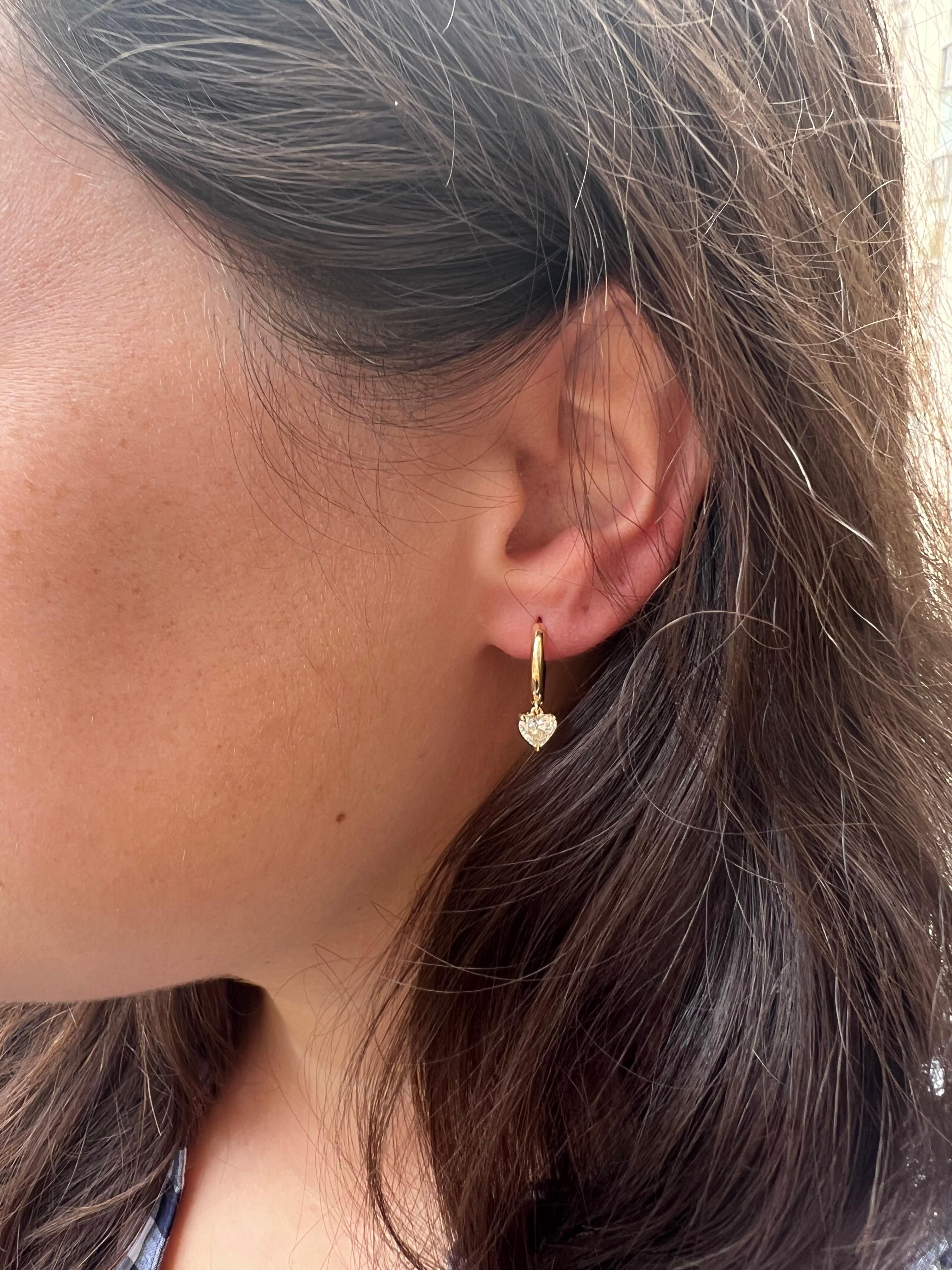 These charming earrings by J. Birnbach are perfect for everyday, worn on their own or part of an ear party! The tubular 18K yellow round round huggies are 1.25 centimeters. A 0.50 carat D color, SI1 clarity heart shape diamond dangles from each