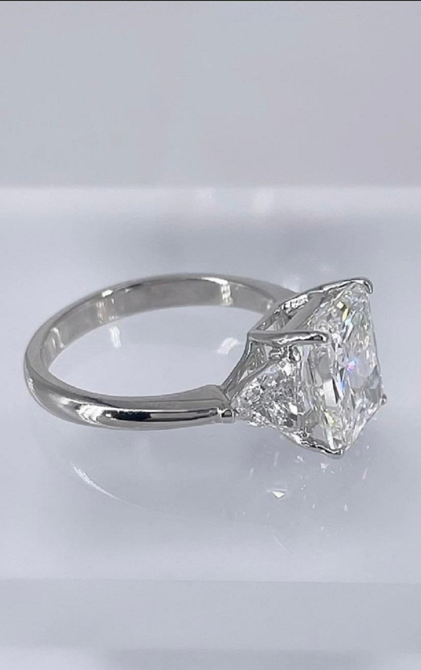 This sparkling three stone ring by J. Birnbach features a 3.21 carat radiant cut diamond, certified by GIA as I color and VS2 clarity. The center diamond is accented by two trillion cut diamonds which total 0.81 carats. The radiant cut is