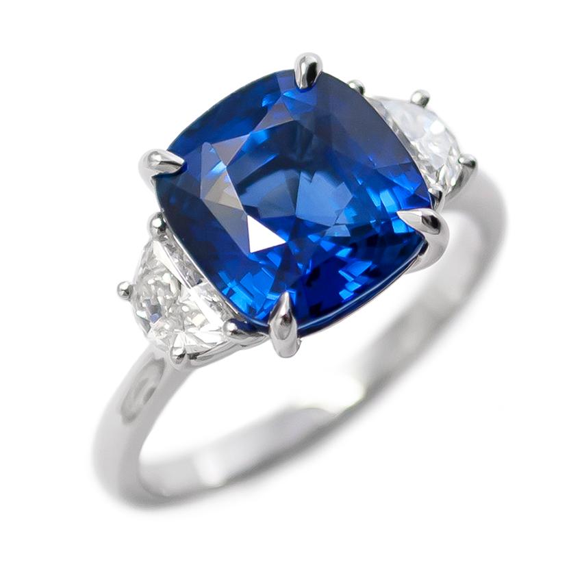 This elegant ring fresh from the J. Birnbach workshop features a vivid and mesmerizing 5.06 ct Sapphire cushion. Set in a handmade, three-stone ring with half moon side stones = 0.55 ctw of G color and VS clarity, this ring is another fantastic
