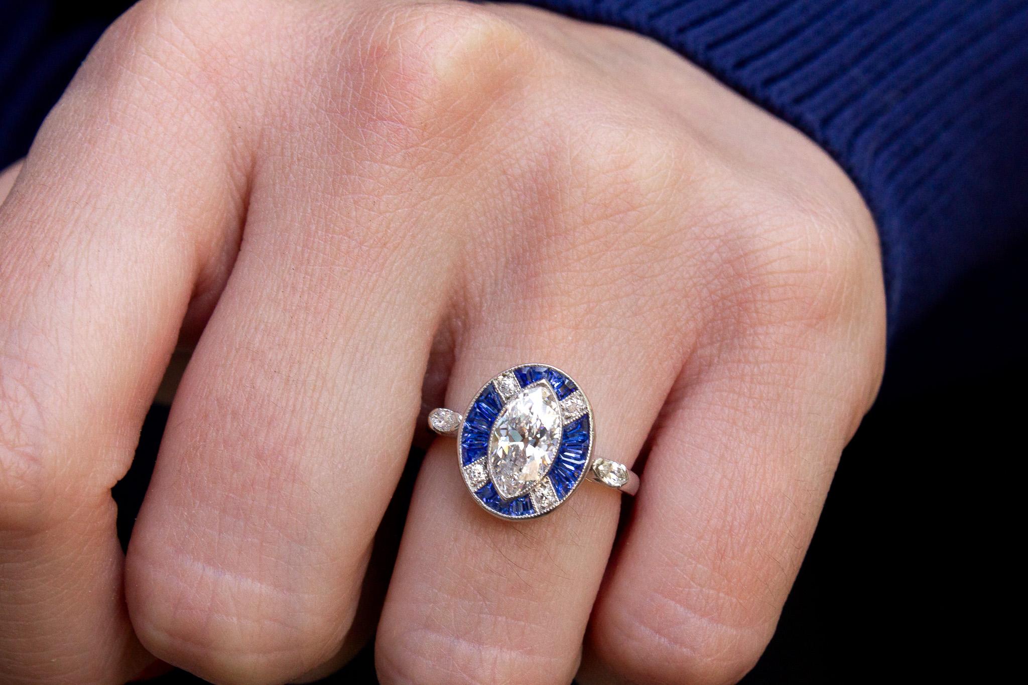 Embrace timeless elegance with this Antique Platinum Art Deco Ring, featuring a captivating marquise diamond framed by a sapphire and diamond halo. At the heart of this antique piece lies a 1.20 carat marquise diamond, boasting E color and SI1