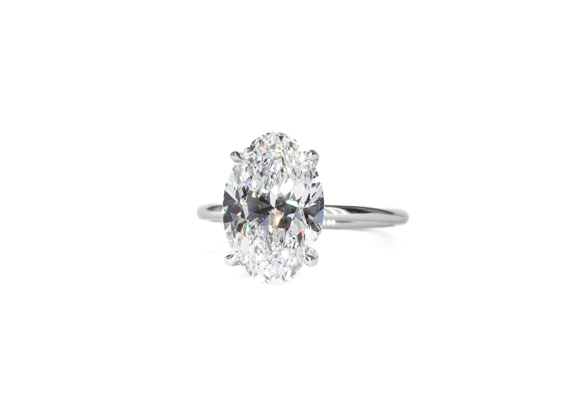 This exquisite platinum solitaire ring is a true embodiment of timeless elegance and sophistication. Featuring a breathtaking 3.82 carat oval cut diamond, graded D SI1 by GIA, the center stone dazzles with exceptional brilliance and a pristine,