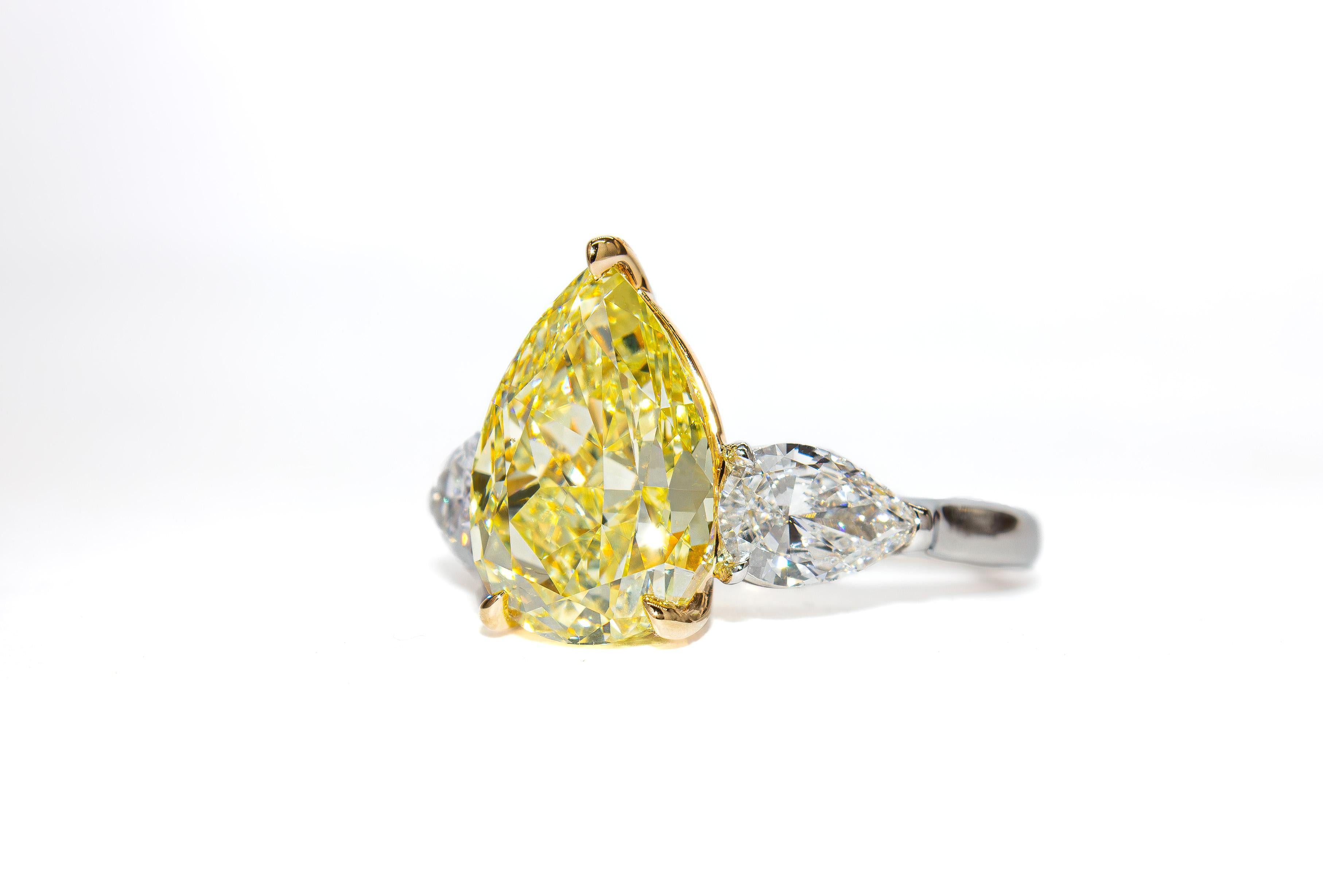 Questo splendido anello a tre pietre combina un'eleganza senza tempo con un colore audace. Realizzato in platino e oro giallo 18 carati, l'anello presenta un vibrante diamante Fancy Yellow a forma di pera da 4,67 carati, certificato da GIA con