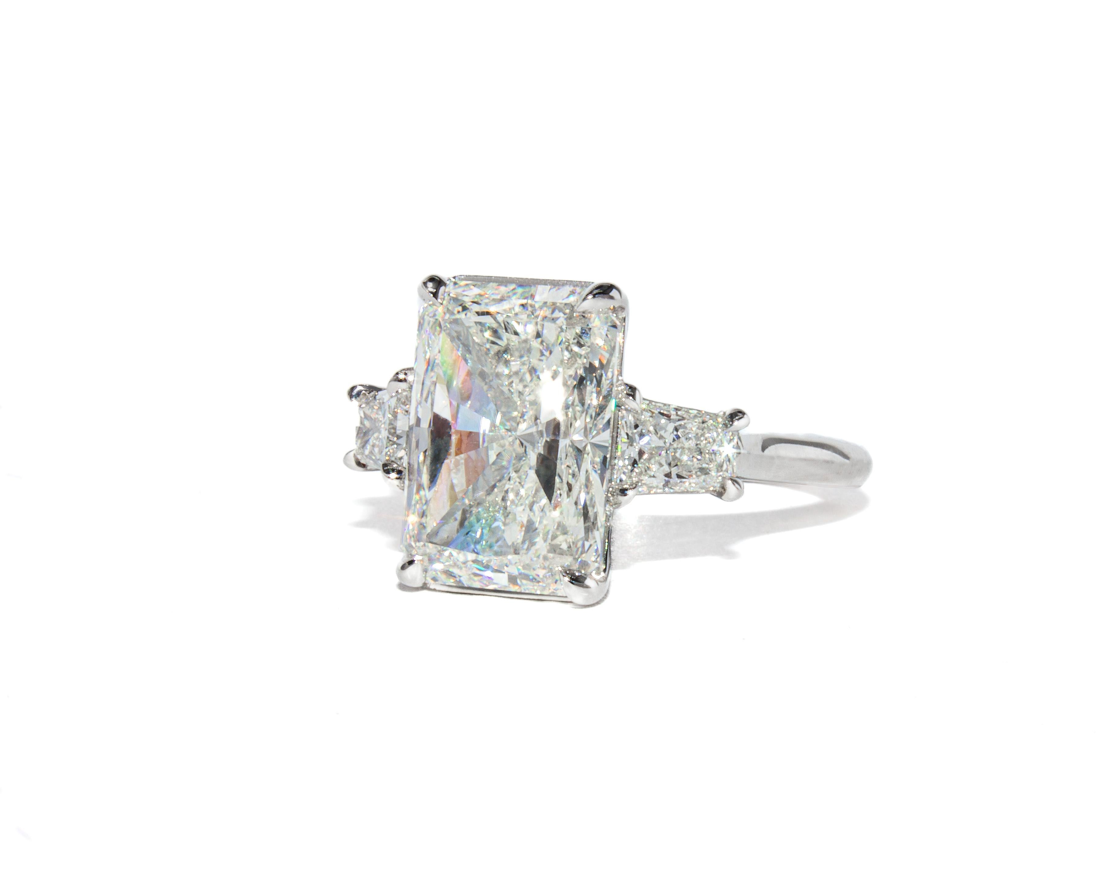 Espressione audace di una raffinatezza senza tempo, questo anello a tre pietre in platino è incentrato su uno splendido diamante a taglio radiante da 5,01 carati, certificato da GIA con colore I e purezza SI2. La pietra centrale è straordinariamente