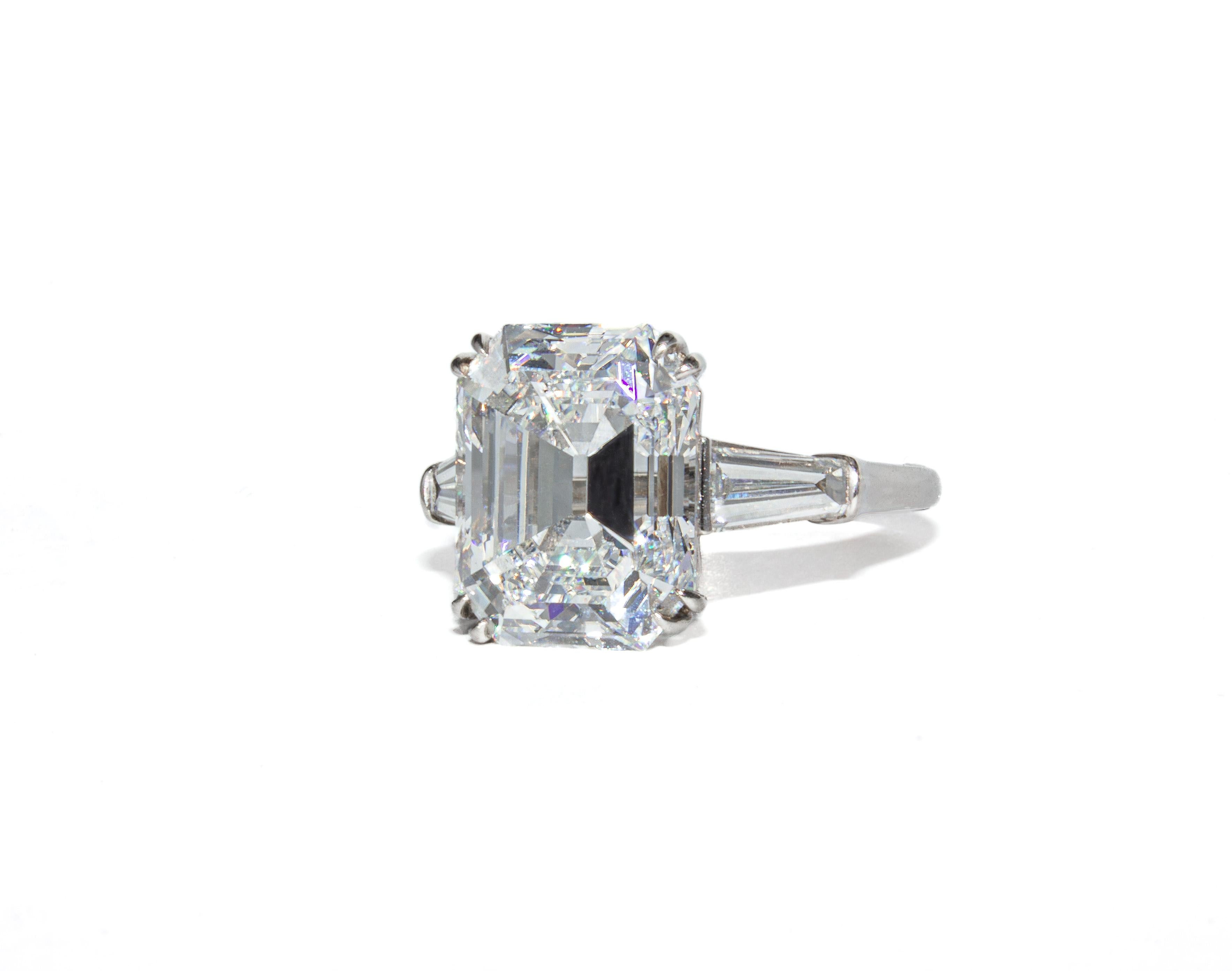 Équilibre raffiné entre élégance et ampleur, cette bague à trois pierres en platine signée J. Birnbach présente en son centre un remarquable diamant taille émeraude de 7,82 carats. Classée de couleur E et de pureté SI2 par le GIA, la pierre centrale