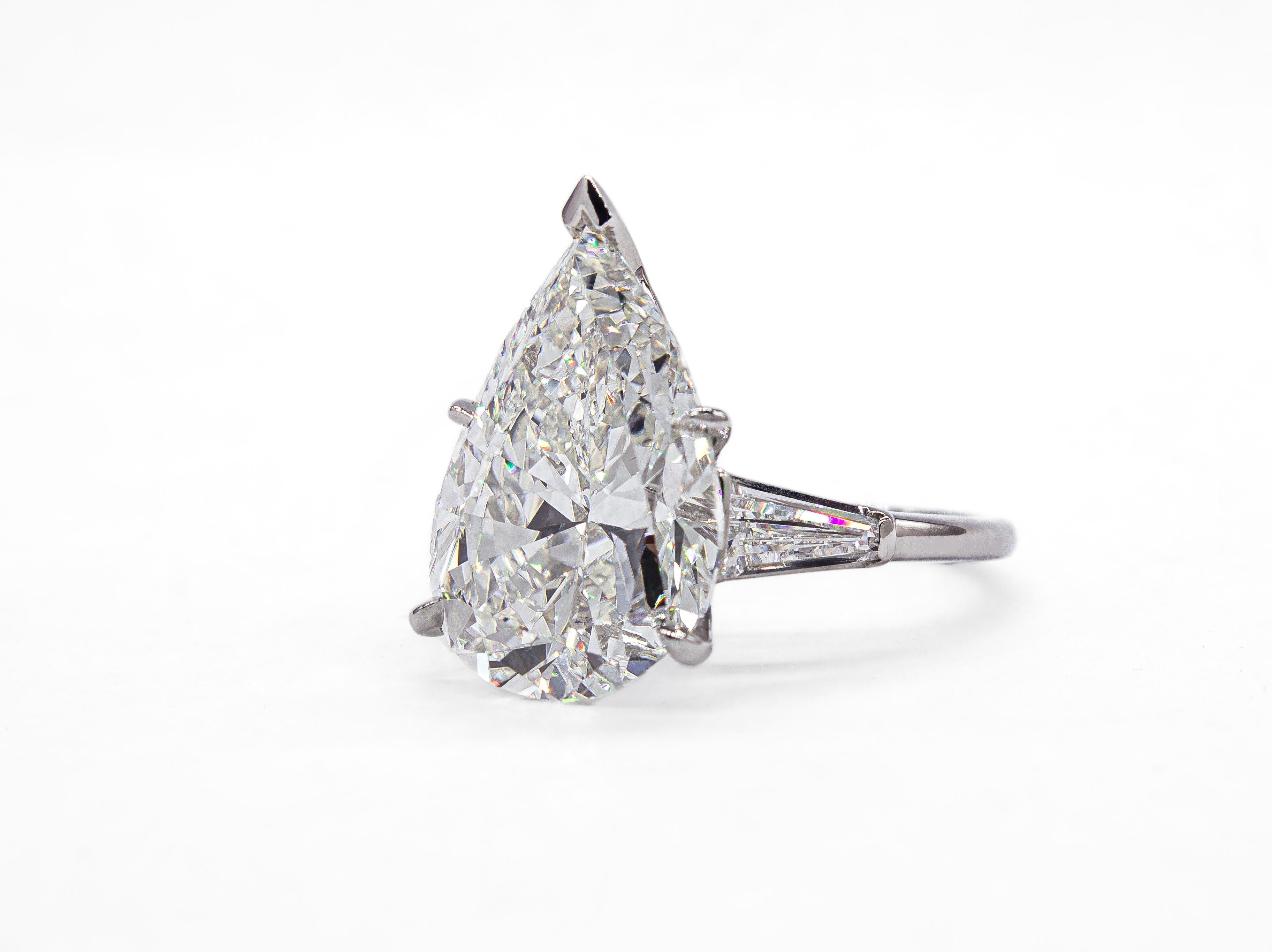 Cette époustouflante bague à trois pierres en platine met en valeur un spectaculaire diamant poire de 9,18 carats en son centre, certifié par le GIA de couleur H et de pureté SI1. La coupe poire allongée offre une silhouette flatteuse et un éclat