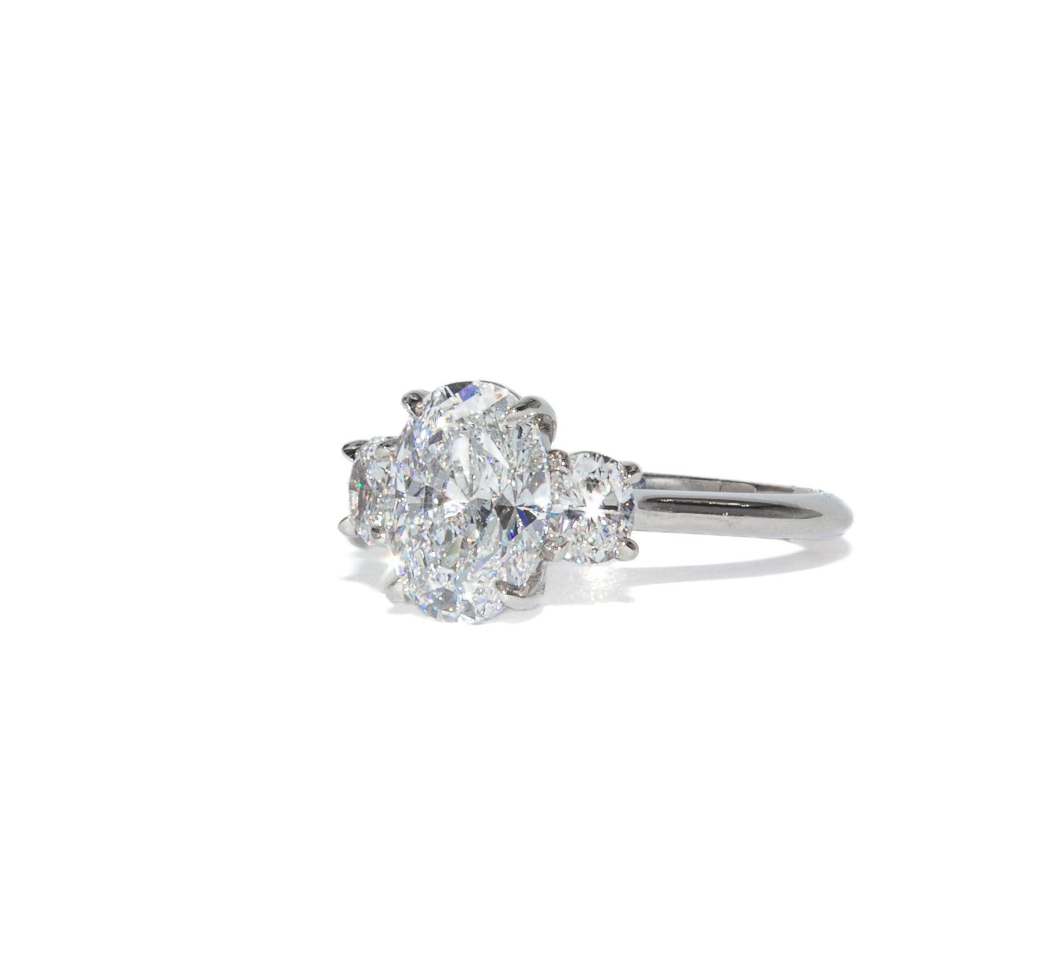 Im Mittelpunkt dieses klassischen Platinrings mit drei Steinen steht ein atemberaubender Diamant mit 1,70 Karat im ovalen Brillantschliff, der von GIA mit der Farbe D und der Reinheit VS1 eingestuft wurde - wahrhaftig die höchste Farbe und eine